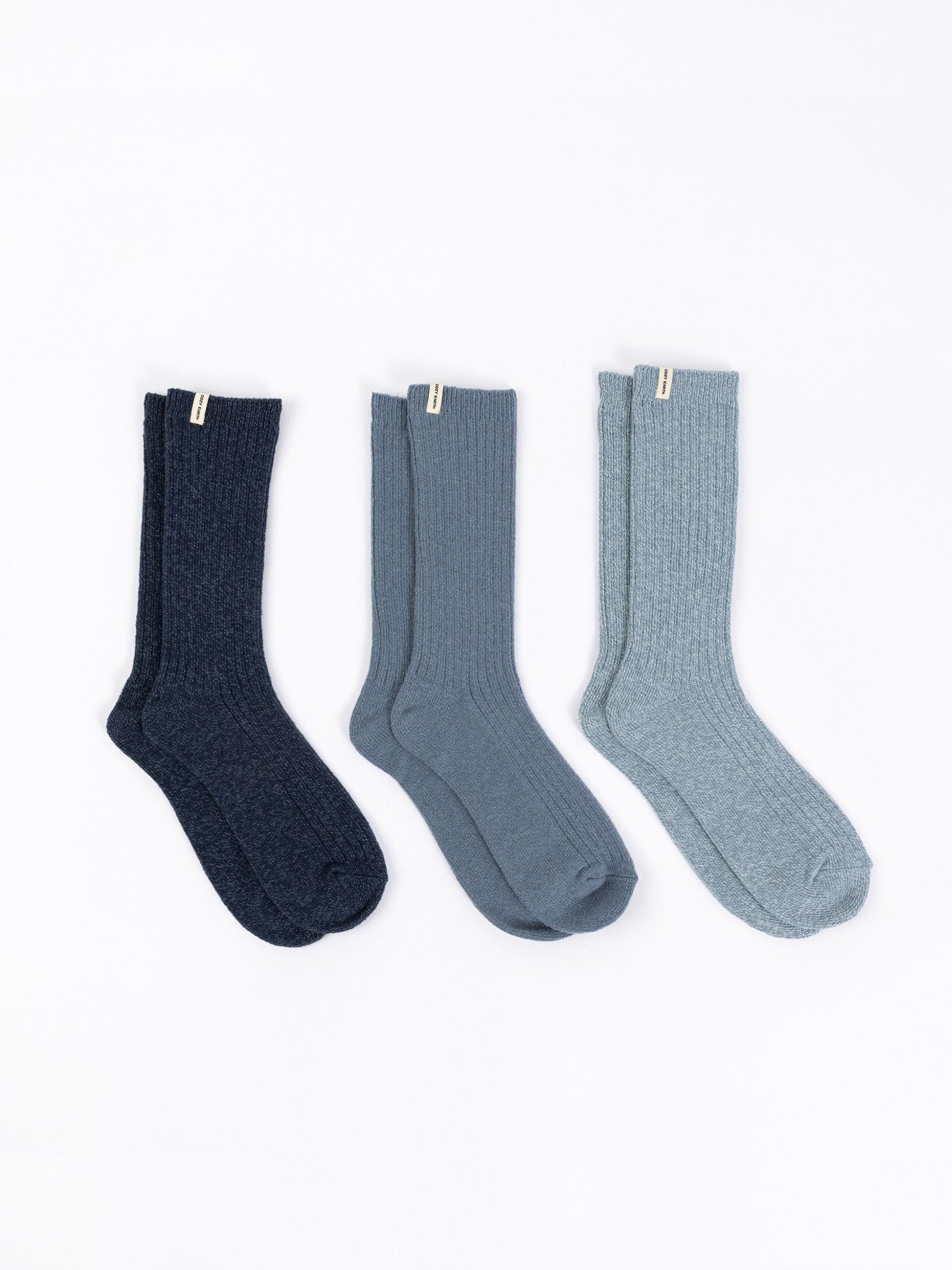 A set of The Plush Lounge Sock 3-Pack by Cozy Earth, featuring three pairs in various blue tones, is stylishly displayed on a white background, each with a small tag near the cuff. 