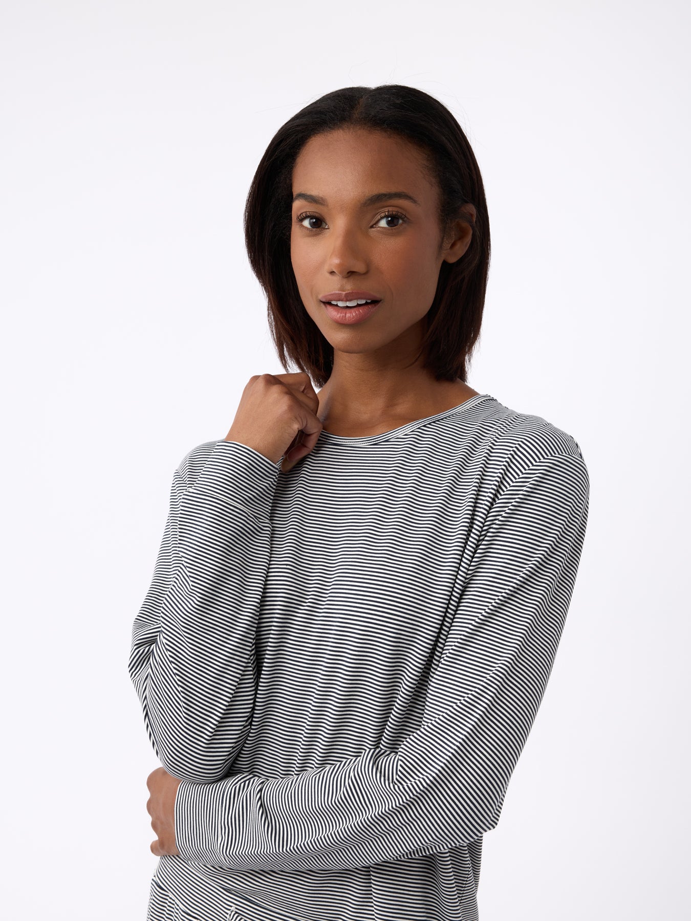 A woman with shoulder-length hair wears a Cozy Earth Women's Bamboo Stretch-Knit Long Sleeve Lounge Tee in black-and-white stripes. Facing forward, she gently rests one hand near her neck with a neutral expression against a plain white background. 