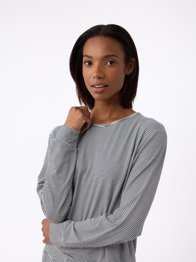 A woman with shoulder-length hair wears a Cozy Earth Women's Bamboo Stretch-Knit Long Sleeve Lounge Tee in black-and-white stripes. Facing forward, she gently rests one hand near her neck with a neutral expression against a plain white background.