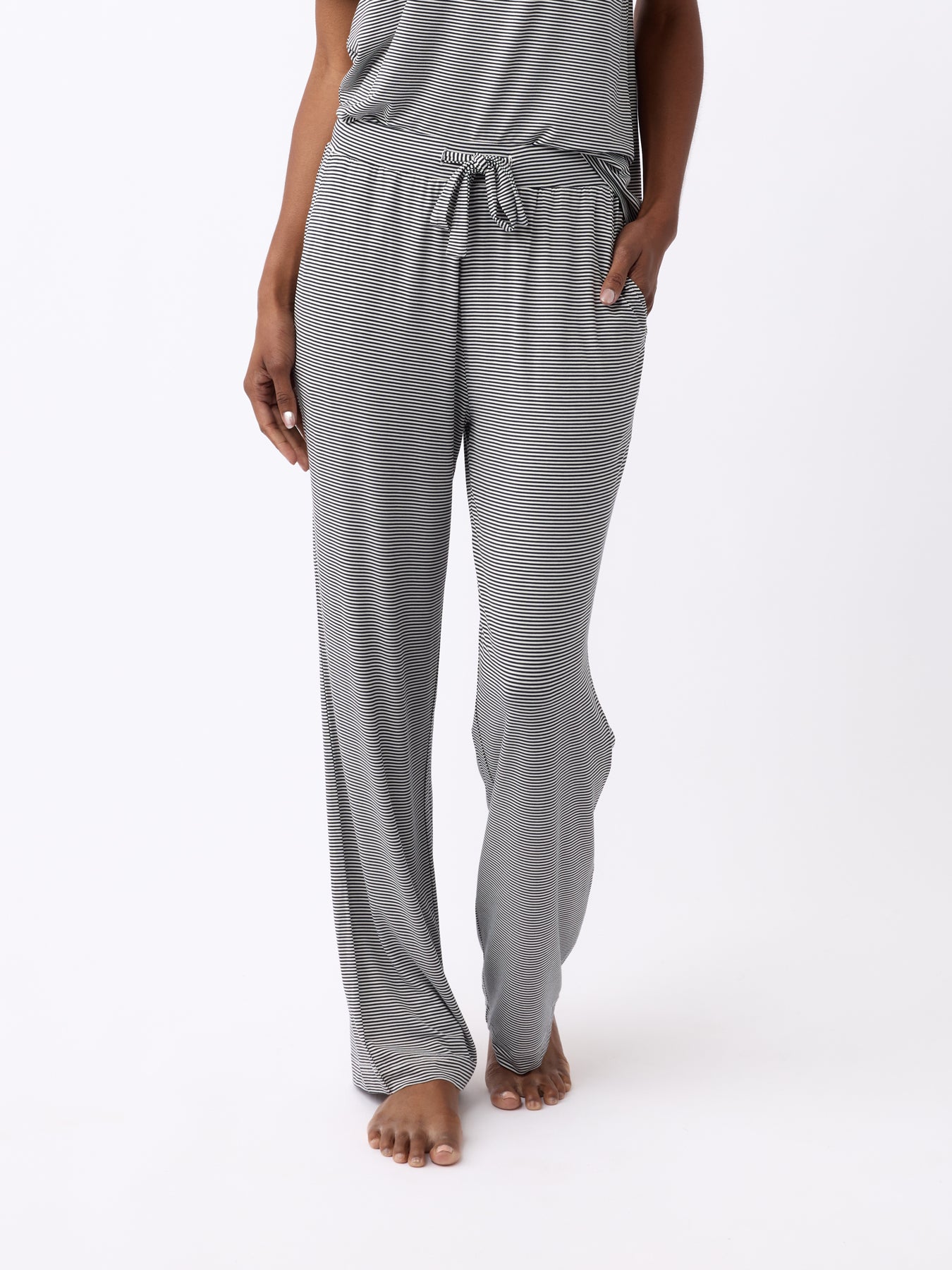 A person is standing barefoot against a white background, wearing Cozy Earth's Women's Bamboo Stretch-Knit Pant in a gray-striped design with a drawstring waist and relaxed fit for comfort. 