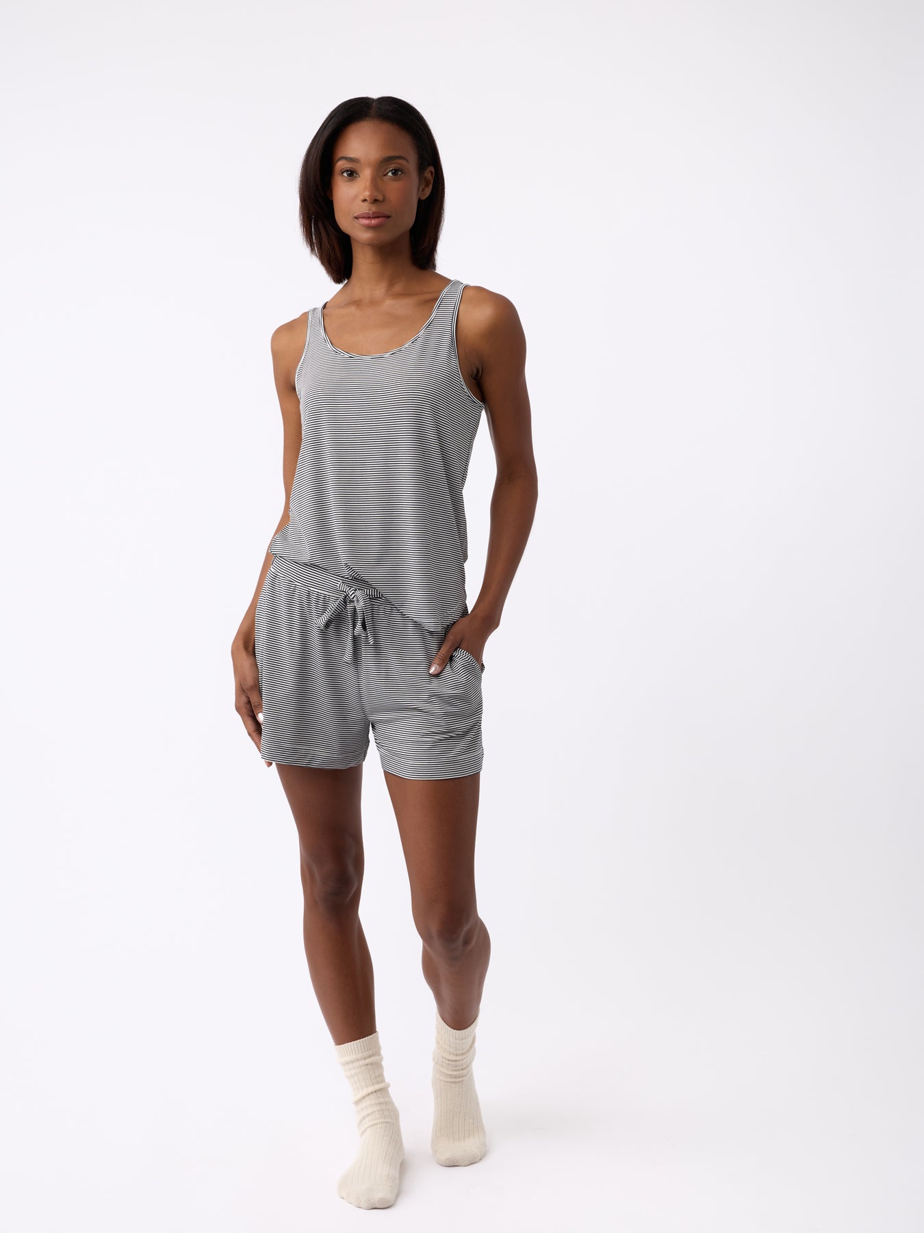 A person is wearing Cozy Earth's Women's Bamboo Stretch-Knit Lounge Tank and shorts. They have their right hand in their pocket, paired with light-colored socks, against a plain white background. 