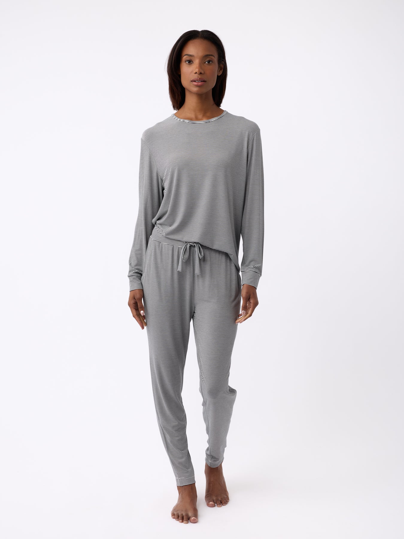 Against a white backdrop, a person barefoot sports the Cozy Earth set, featuring the Women's Bamboo Stretch-Knit Tapered Pant in grey. The outfit exudes comfort and relaxation. 