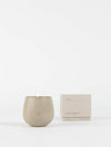 A beige ceramic Candle EMBER from Cozy Earth with a small flame is displayed beside its matching beige box labeled "Cozy Earth" on a white background.