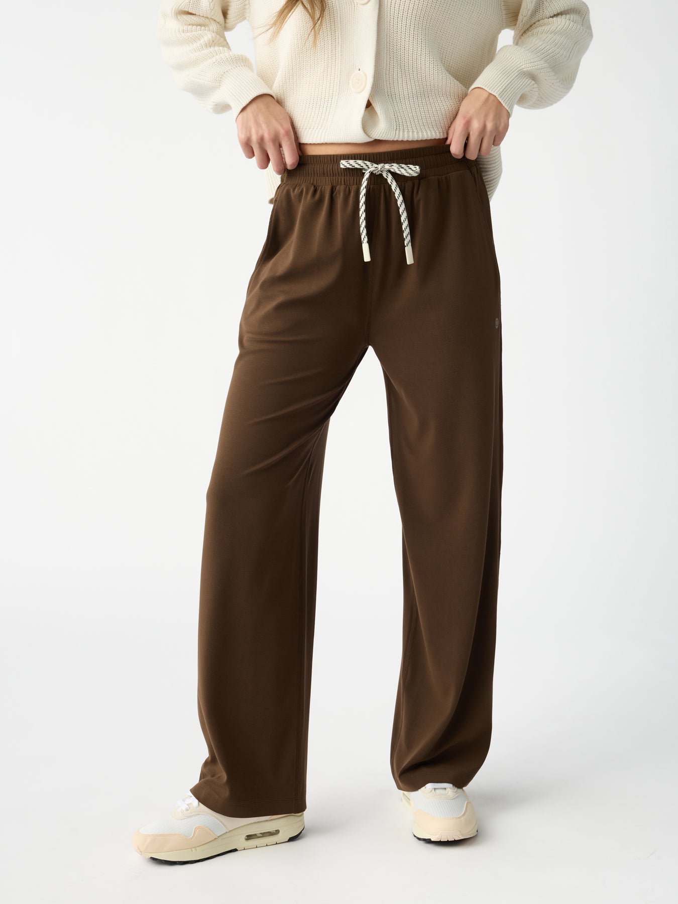 A person in Cozy Earth's Women's Studio Wide Leg Pant with a striped tie stands against a plain backdrop. They're wearing a cream sweater and white sneakers, though their upper body is partially out of frame. |Color:Espresso