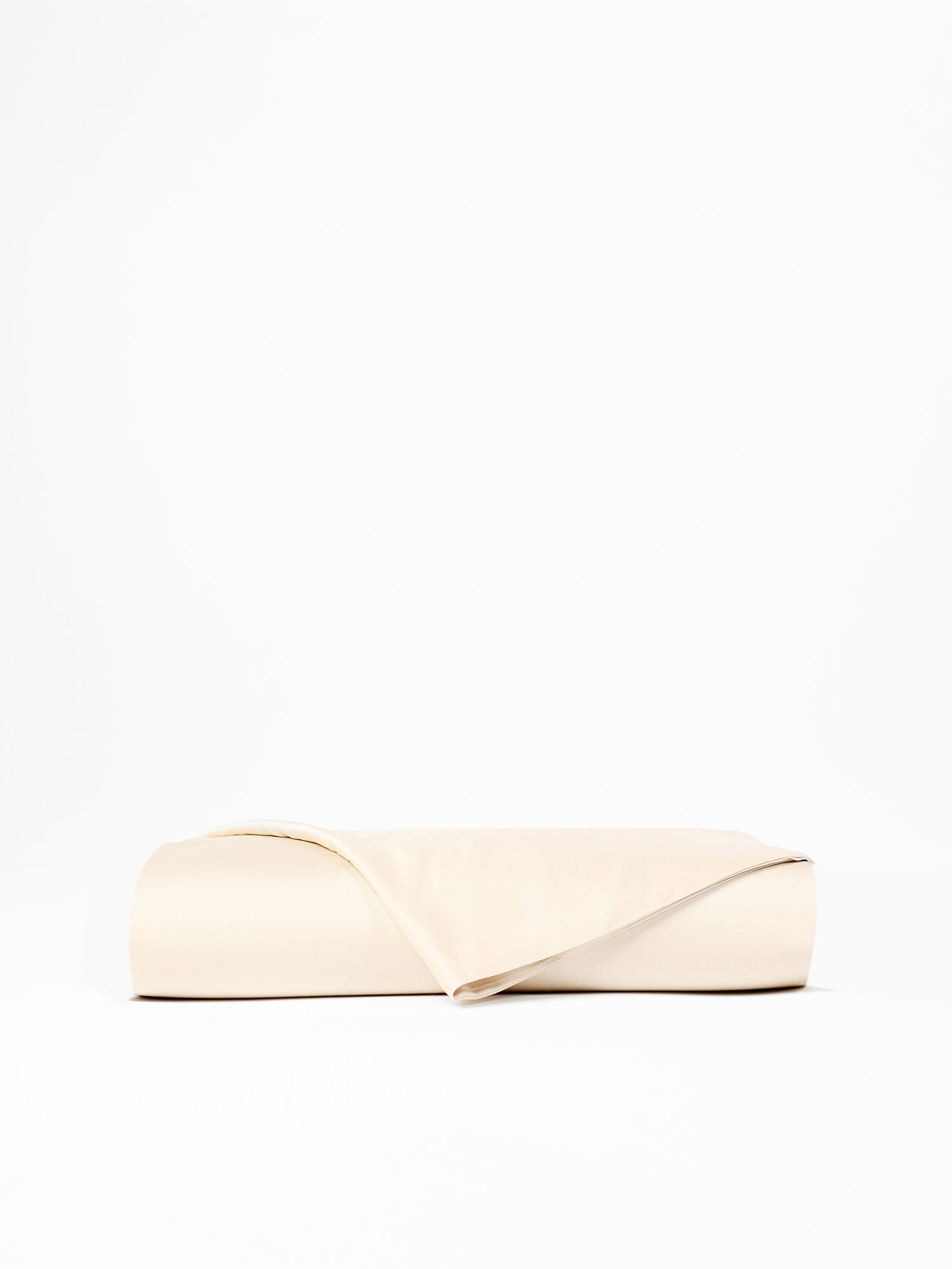 A neatly folded, light beige Bamboo Flat Sheet from Cozy Earth is placed against a plain white backdrop. The corner of the sheet is slightly lifted, revealing its smooth, soft texture. 