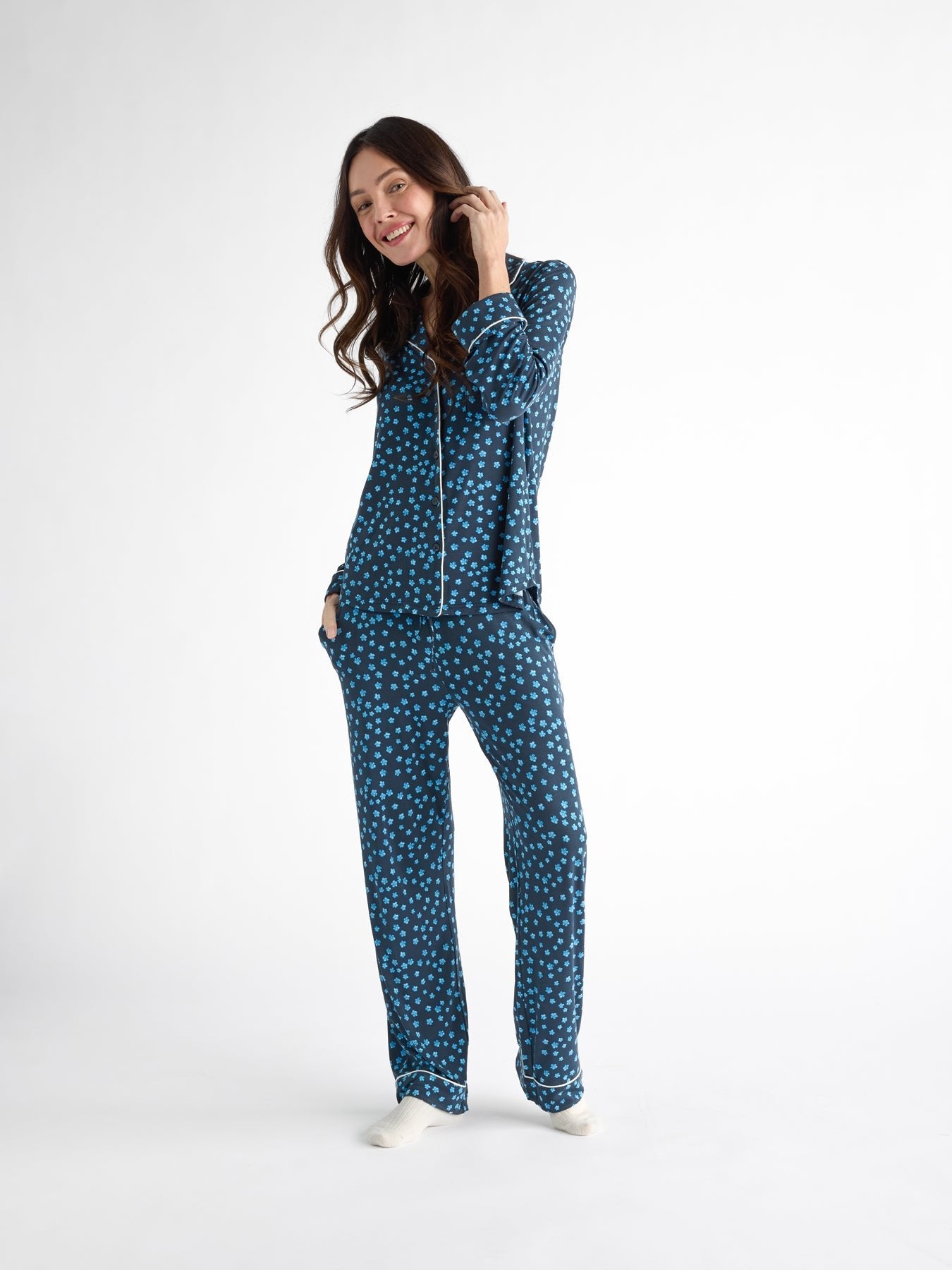 A person with long brown hair smiles on a plain white background wearing Cozy Earth's Women's Bamboo Stretch-Knit Long Sleeve Pajama Set in blue with white polka dots, featuring pockets and long sleeves. |Color:Forget Me Nots