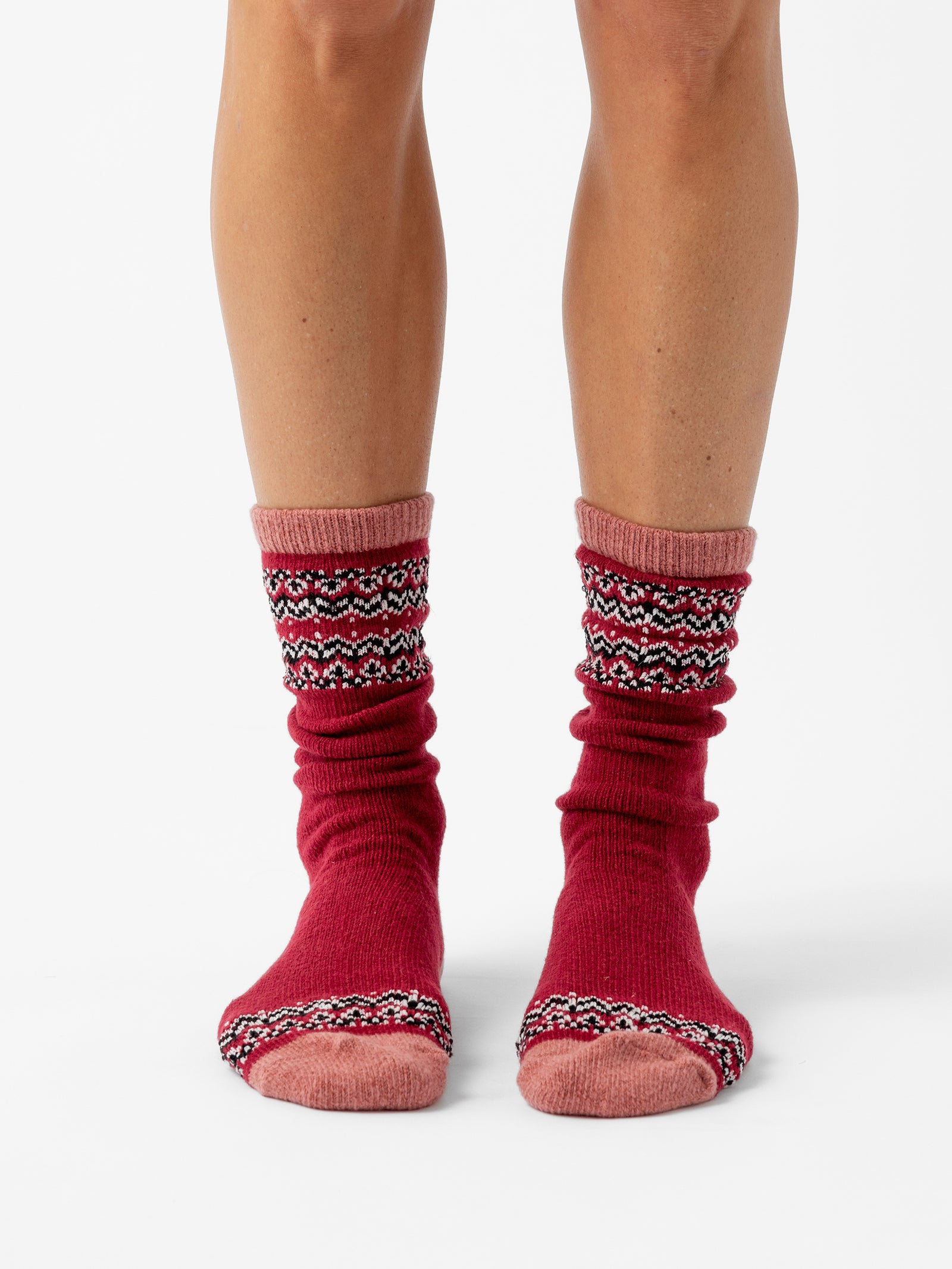 A person stands facing forward in front of a white background wearing Fair Isle Plush Lounge Socks in Garnet. 