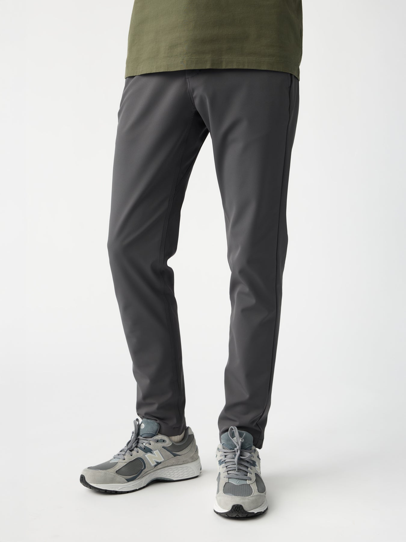 A person stands slightly apart, wearing a green shirt with Cozy Earth's Men's Everywhere Pant in charcoal gray. They sport gray athletic shoes with white soles against a plain white background. |Color:Graphite