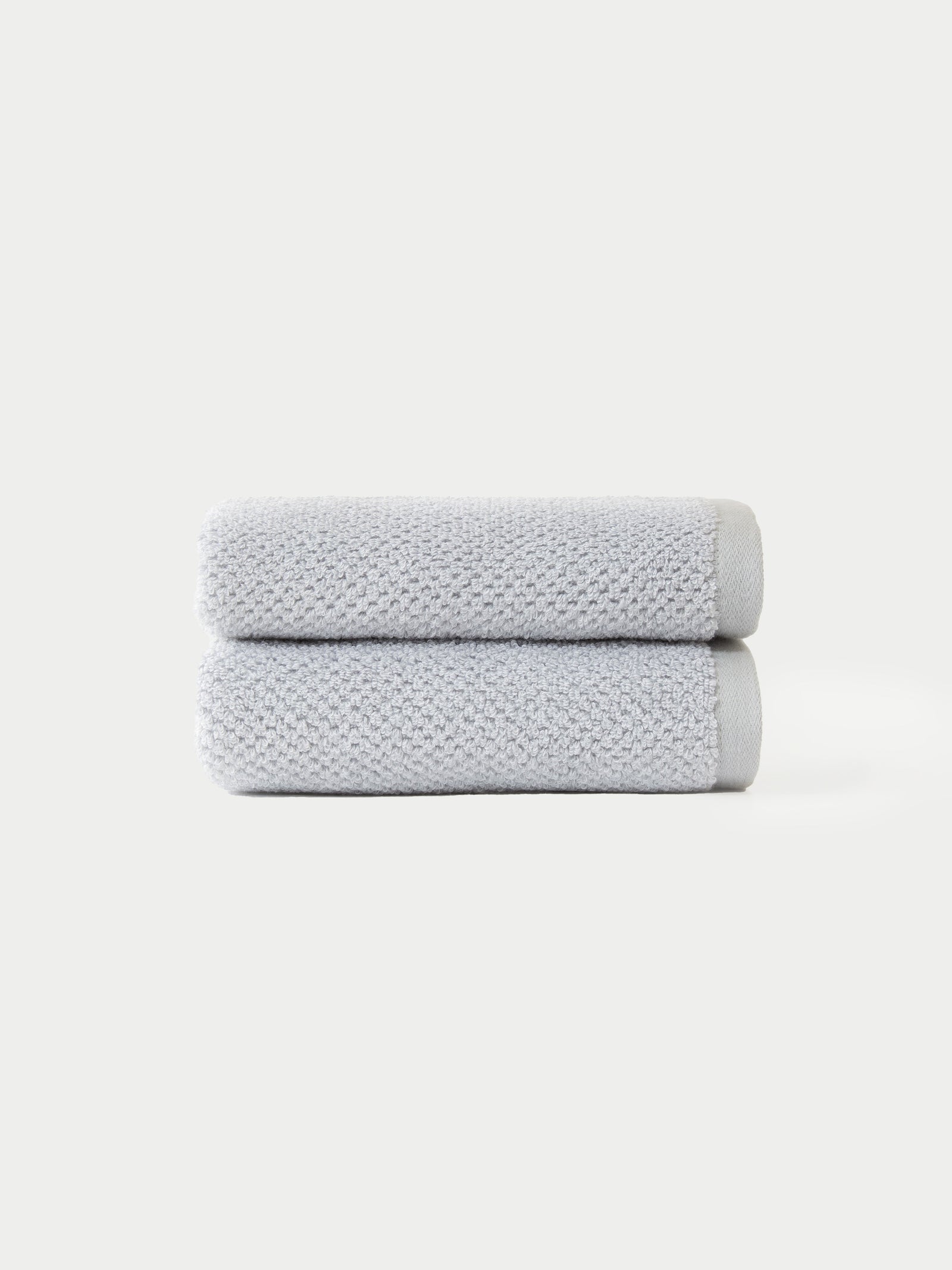 Two Nantucket Bath Towel Set towels by Cozy Earth, neatly folded in light gray and stacked atop each other, displayed against a plain white background.