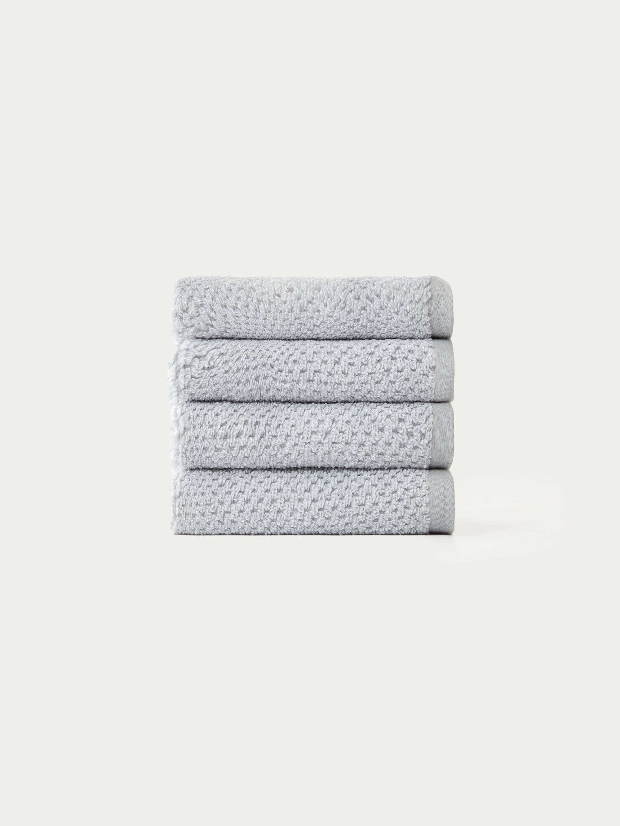 A neatly stacked pile of four light gray, textured towels from the Cozy Earth Nantucket Bath Towel Set on a plain white background.