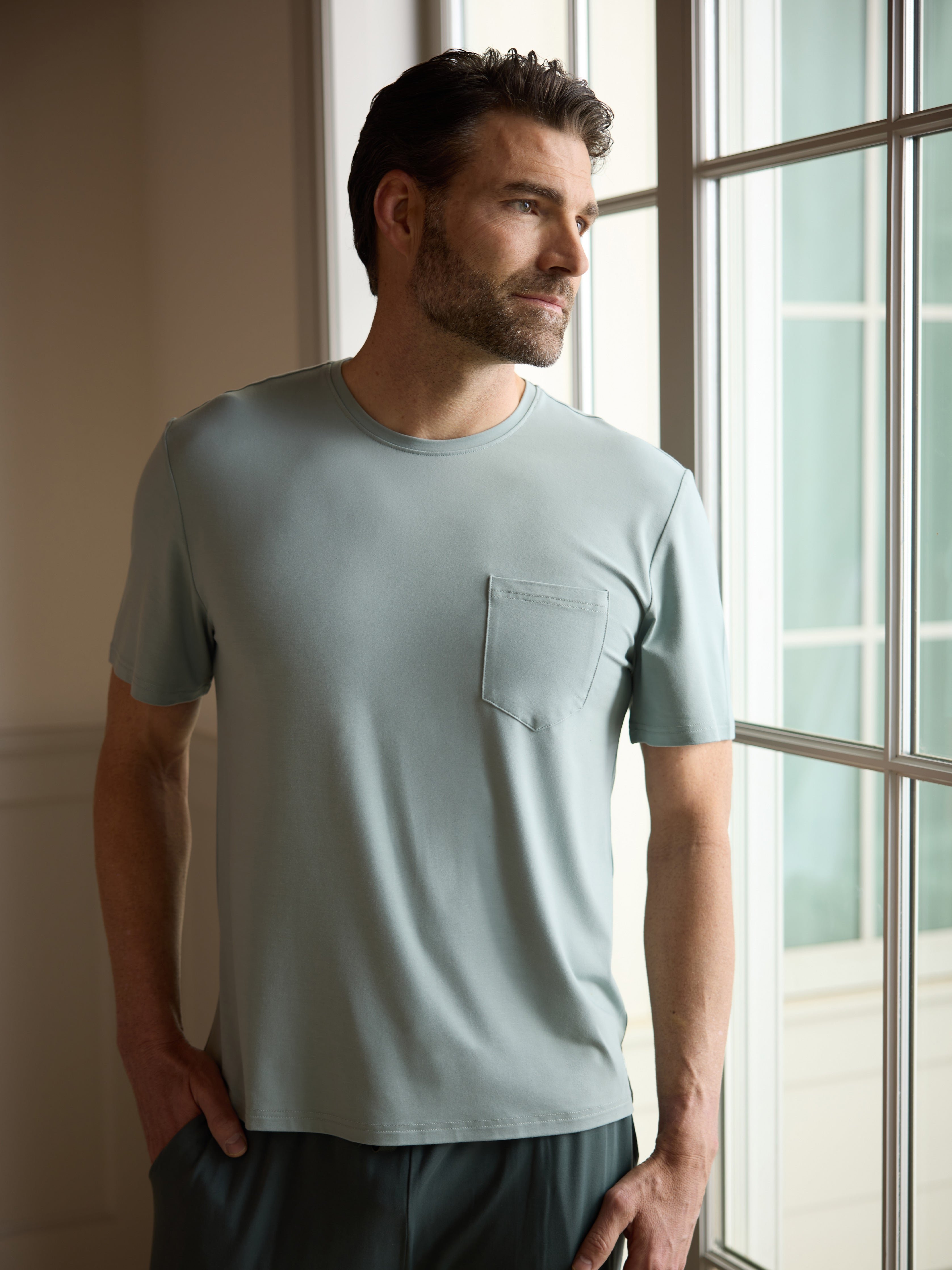 Man wearing haze pajama shirt next to window 