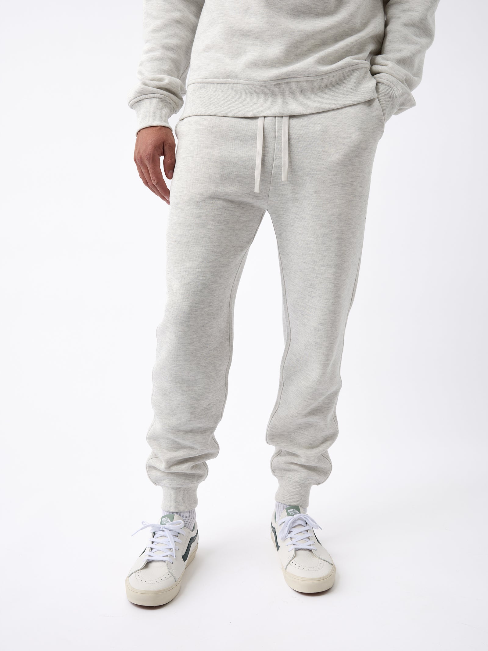 A person wearing the Men's CityScape Jogger in light gray from Cozy Earth, paired with white sneakers, stands against a white background. The outfit looks casual and comfortable. 