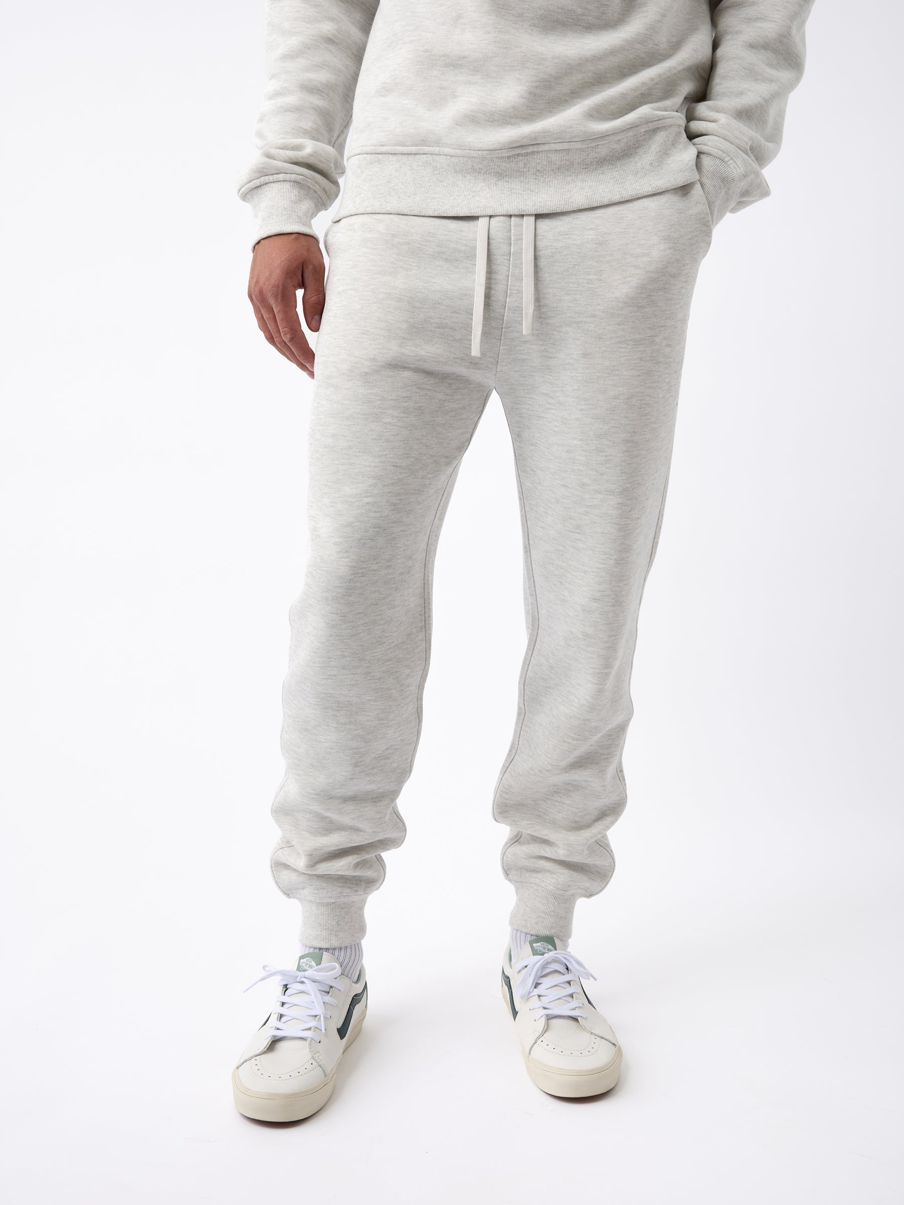 A person wearing the Men's CityScape Jogger in light gray from Cozy Earth, paired with white sneakers, stands against a white background. The outfit looks casual and comfortable. |Color:Heather Grey