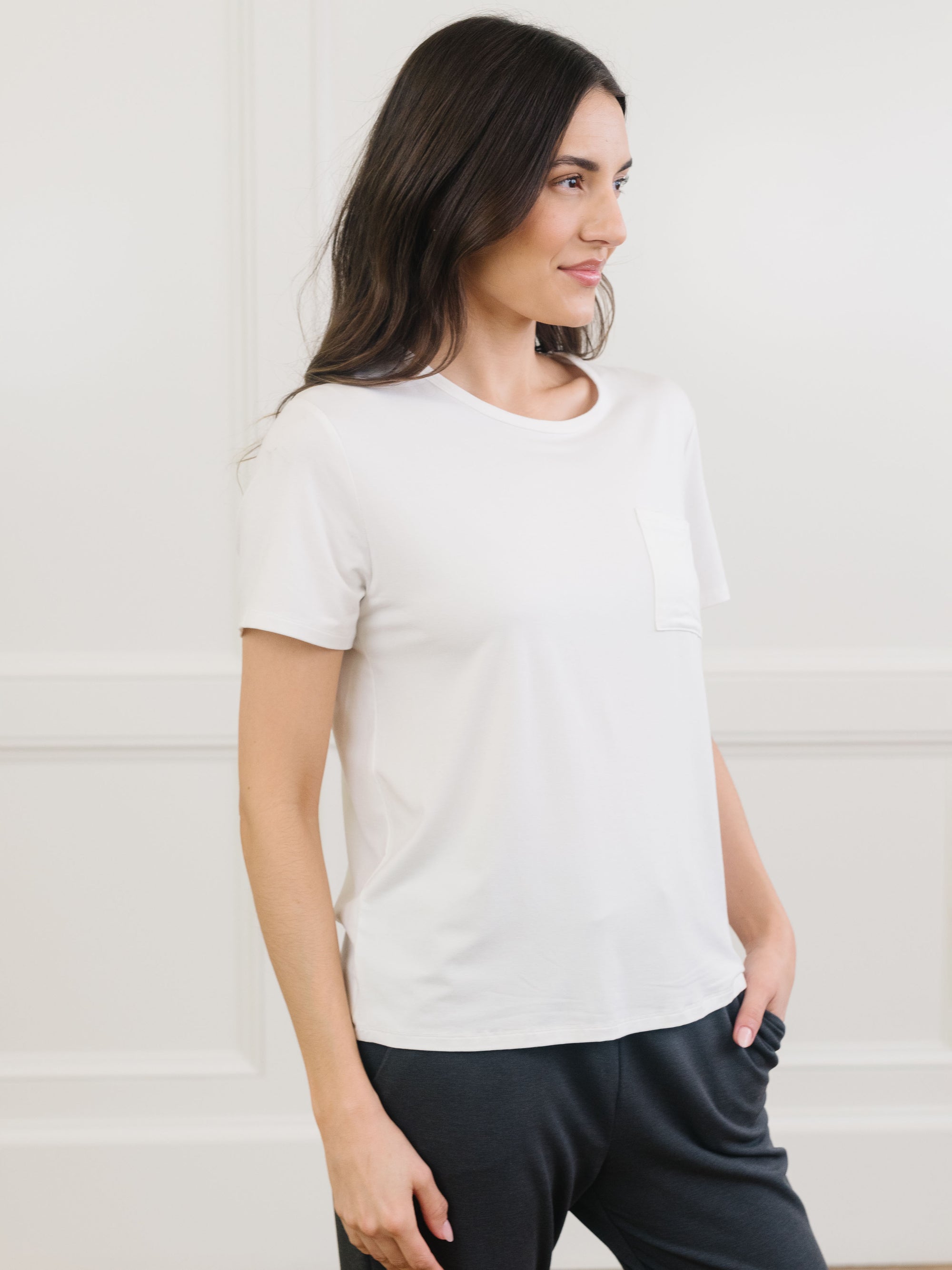 Woman wearing a white t-shirt and dark pants against a light background 