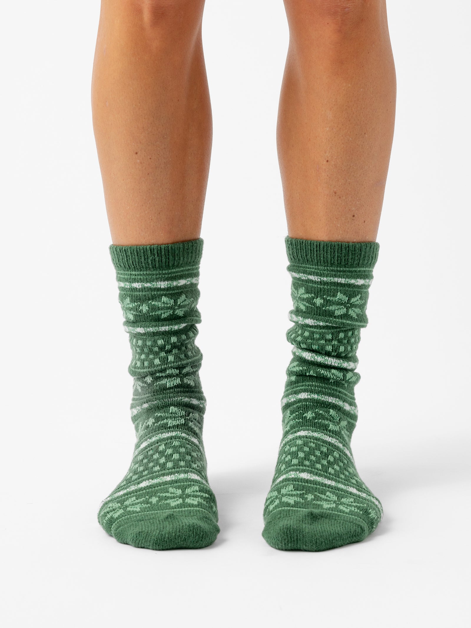 A person stands with a white background wearing Snowflake Plush Lounge Sock in Jade 