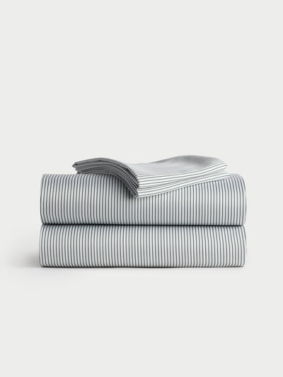 A neatly folded stack of the Bamboo Sheet Set by Cozy Earth, featuring a thin black striped pattern on a white background, is placed on a light grey surface. |Color:Jade Pinstripe