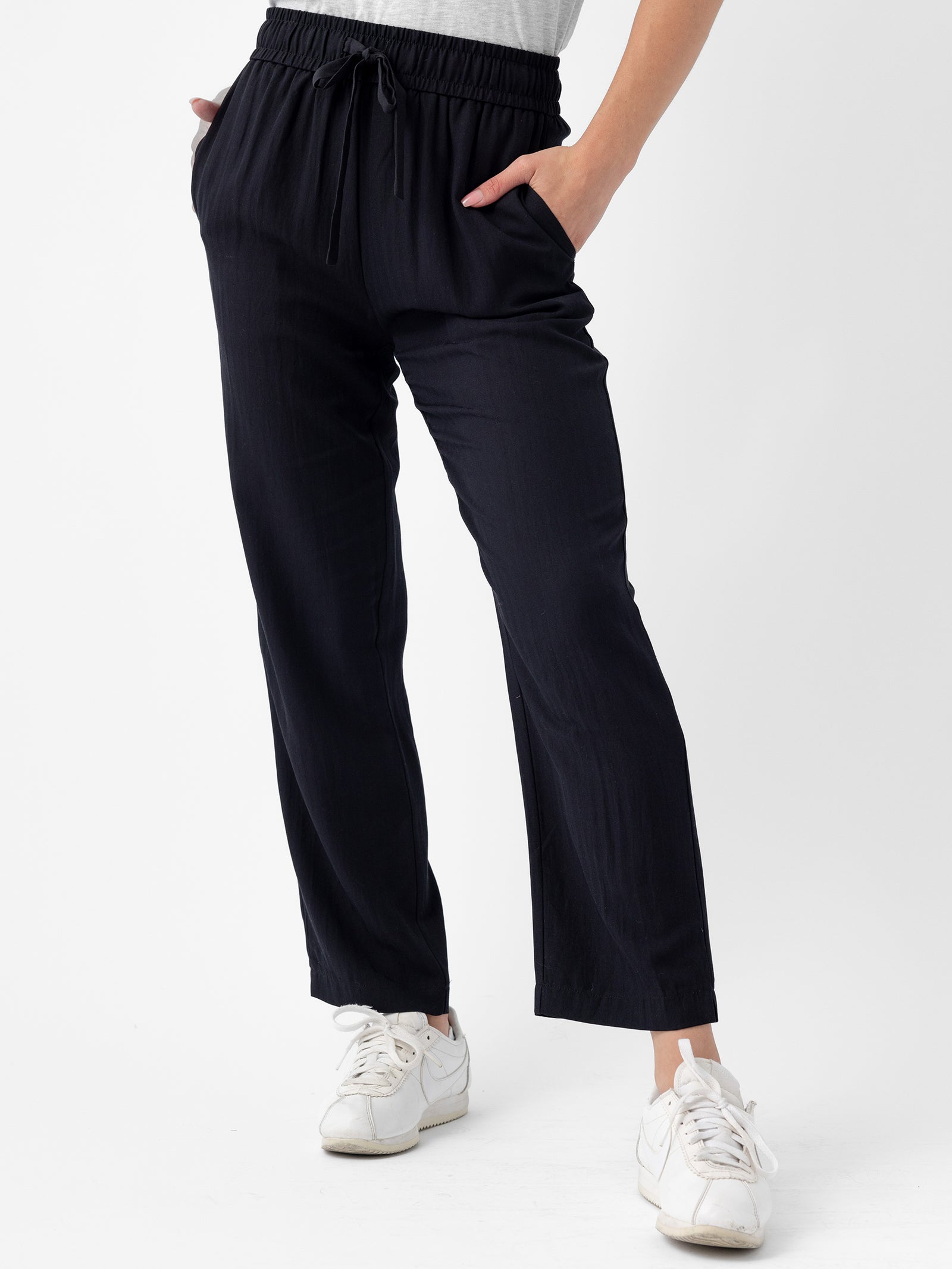 Person wearing Cozy Earth's Women's Sunset Cropped Pant in Jet Black with hands in pockets and white sneakers. The background is plain white. 