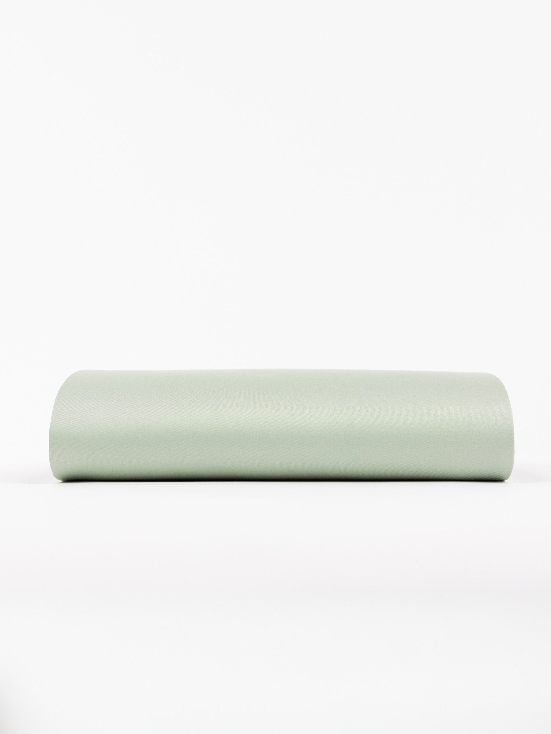 A cylindrical yoga bolster covered in light green fabric rests horizontally on a white surface, offering a minimalist and clean look. 