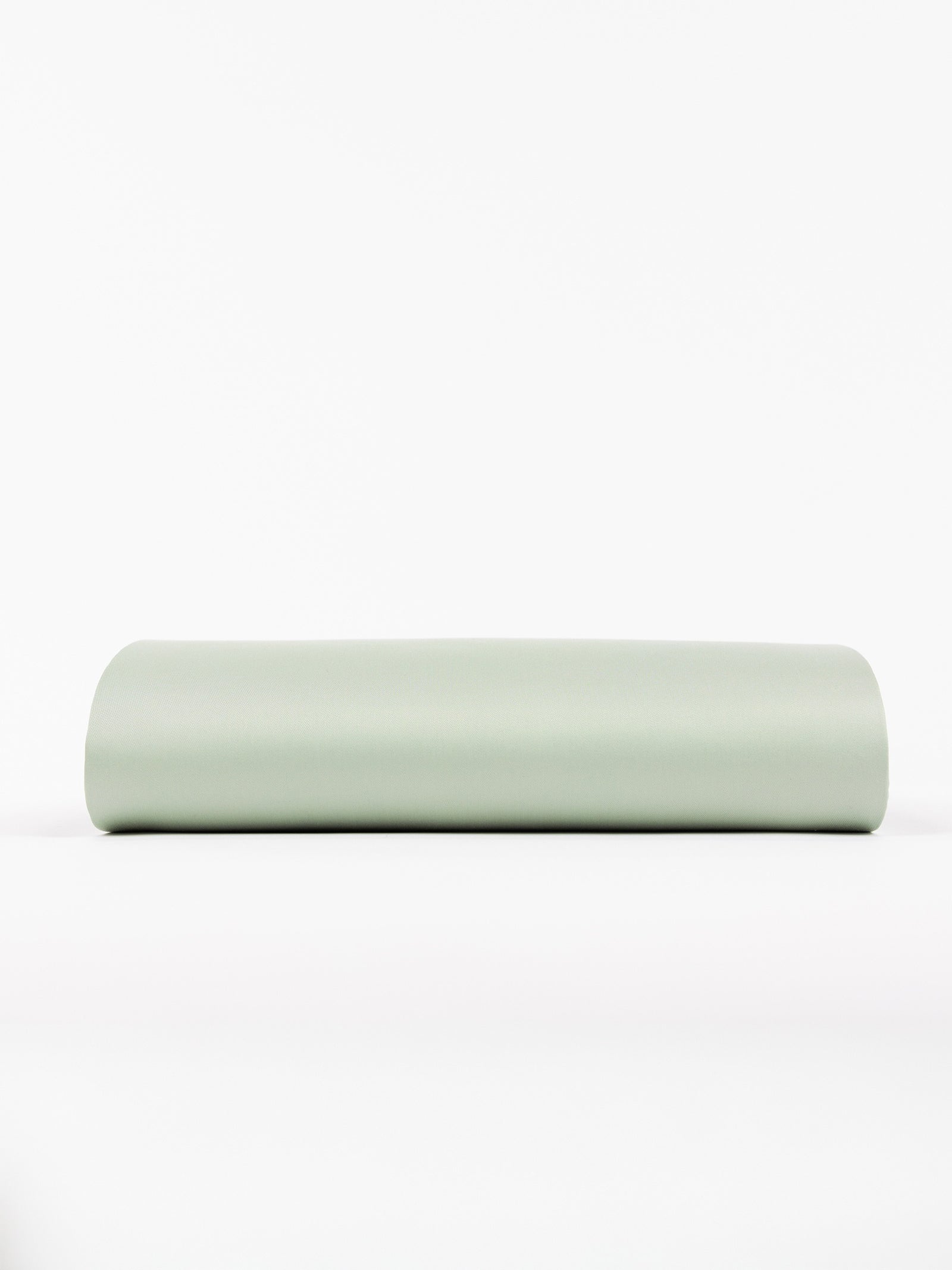 A cylindrical yoga bolster covered in light green fabric rests horizontally on a white surface, offering a minimalist and clean look. 