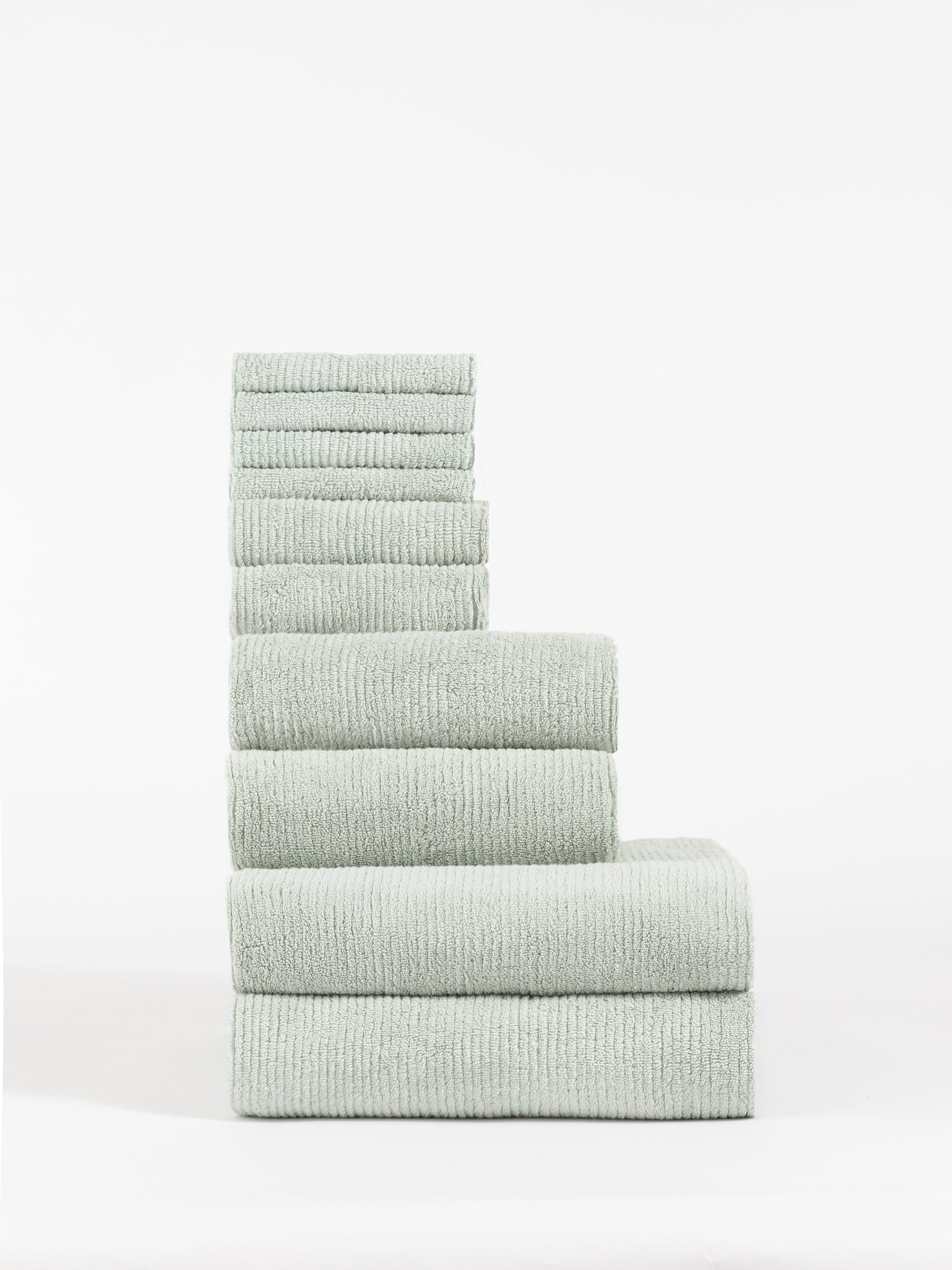 A neatly stacked Ribbed Terry Bath Towel Set by Cozy Earth, featuring a soft, slightly ribbed texture in light green and available in various sizes, arranged vertically against a plain white background. 