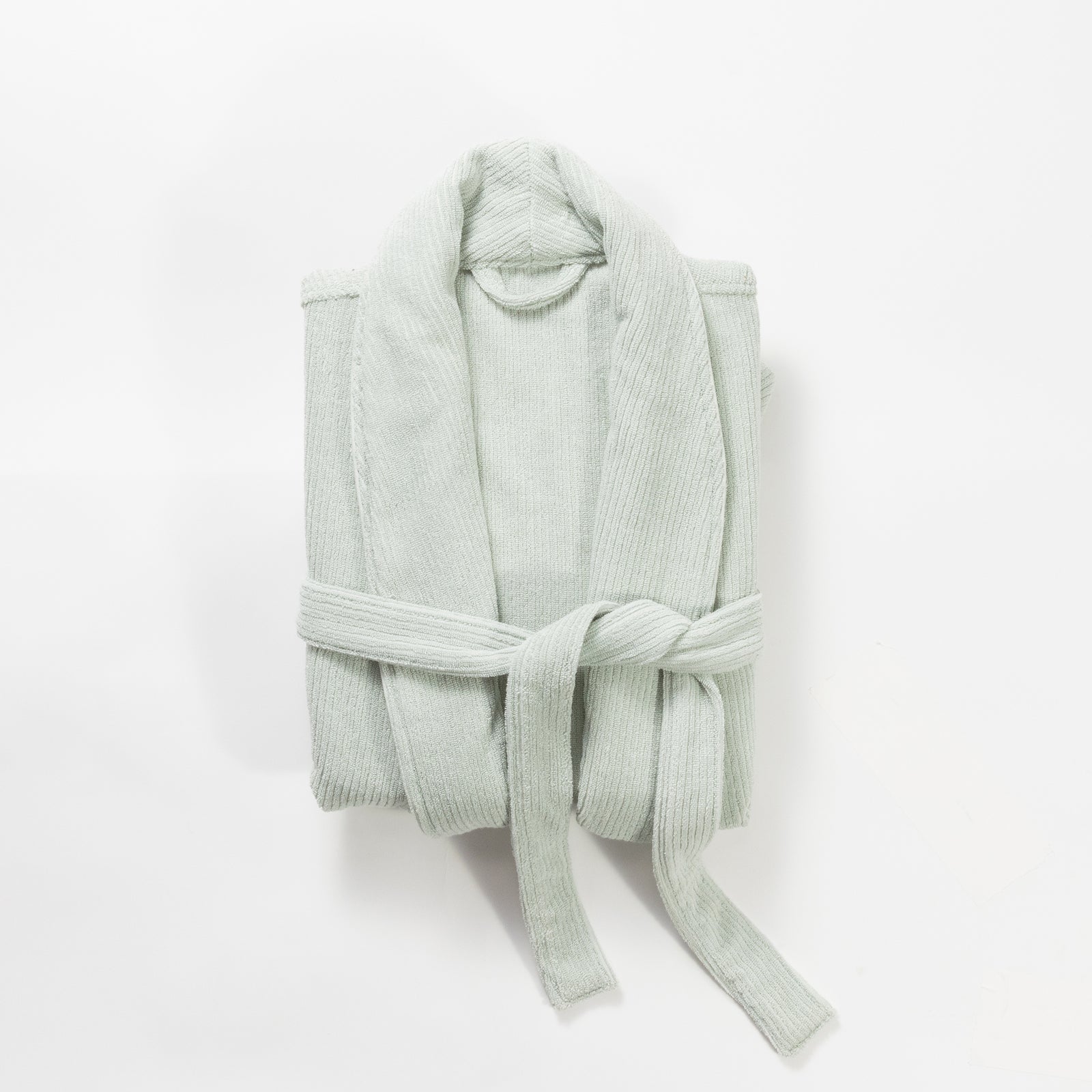 The Ribbed Terry Bath Robe by Cozy Earth is neatly folded and tied with its belt around the middle, creating a tidy, compact appearance. The light gray robe features a soft, textured fabric and a shawl collar, all presented against a plain white background. 