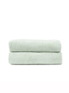 Two Ribbed Terry Bath Towels by Cozy Earth, in light green, are neatly folded and stacked together against a plain white background.|Color:Laurel