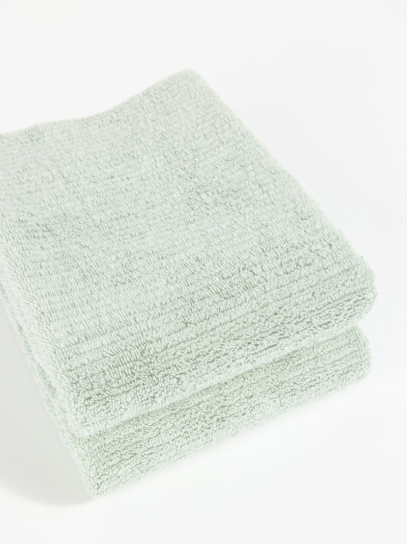 Two Cozy Earth Ribbed Terry Hand Towels in light green are neatly folded and stacked against a white background.
