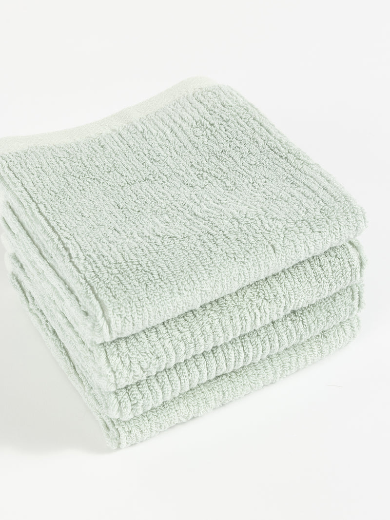 A neatly folded stack of four soft, light green Ribbed Terry Washcloths by Cozy Earth is placed on a white surface. The washcloths have a textured appearance and appear fluffy, suggesting they are absorbent and comfortable for use.
