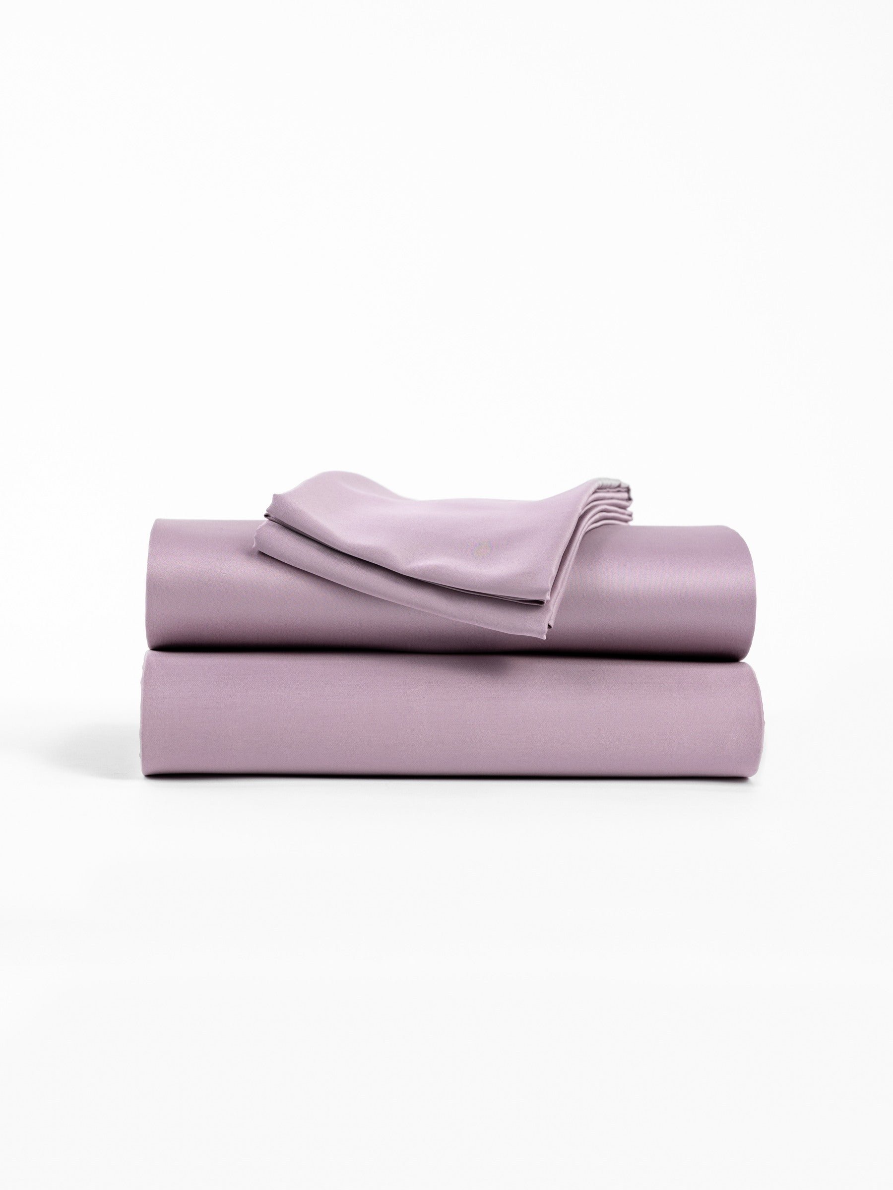A neatly folded stack of Cozy Earth's Bamboo Sheet Set in Lavender, featuring two larger pieces and one smaller piece on top, is displayed against a plain white background. 