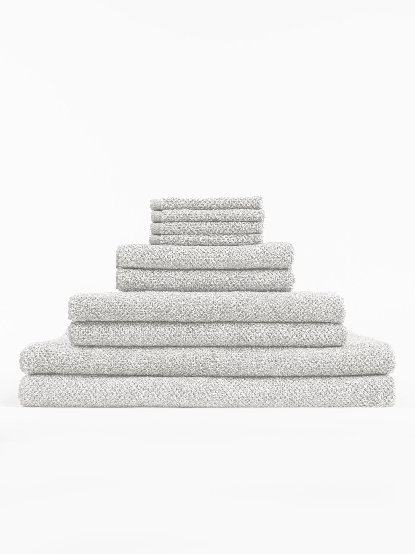 The Cozy Earth Complete Nantucket Bath Bundle features clean, plush light gray towels in various sizes with a textured pattern, neatly stacked in a pyramid shape against a white background.|Color:Heathered Light Grey
