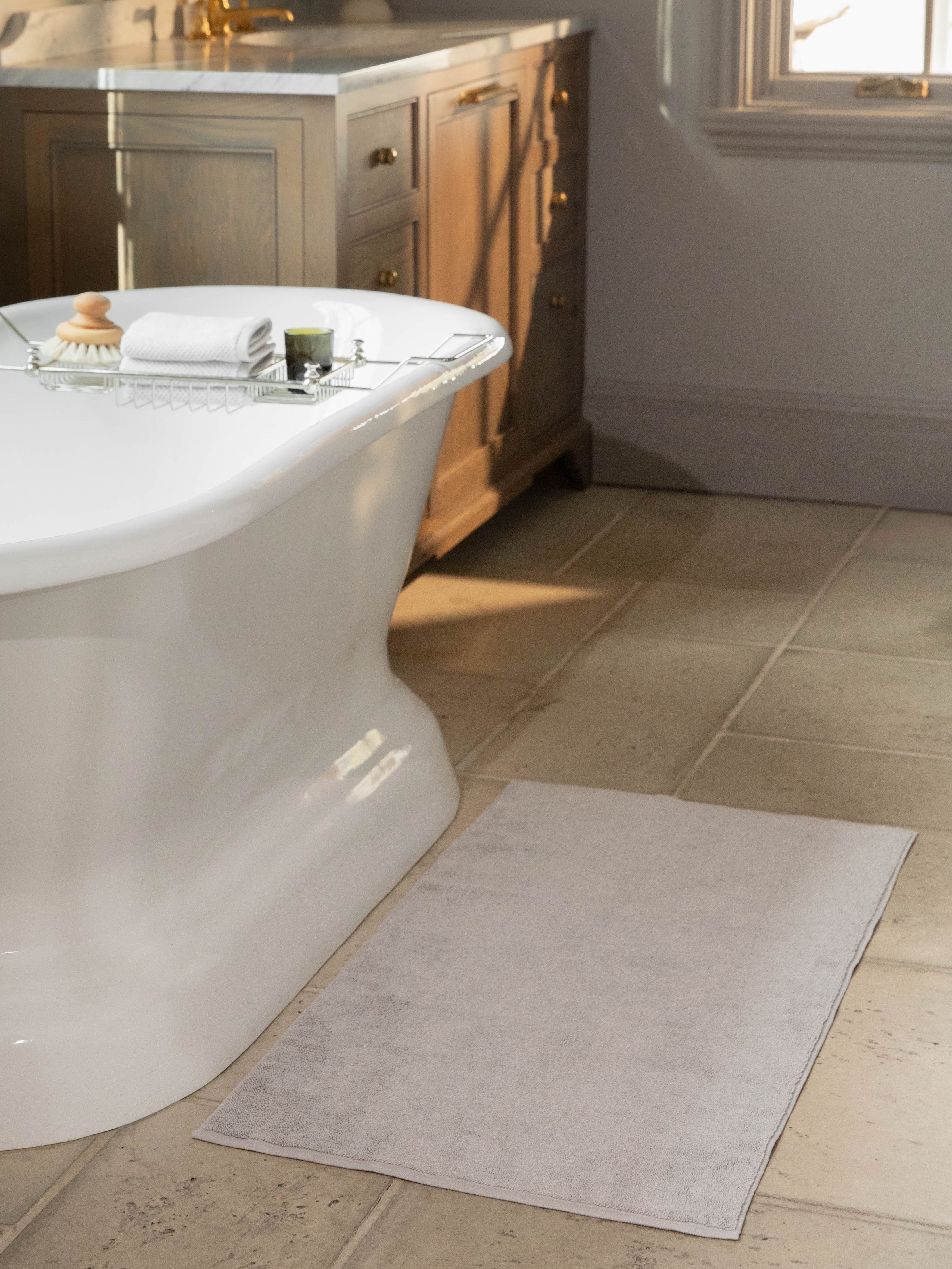 Light Grey bath mat resting on bathroom floor in front of bathtub.