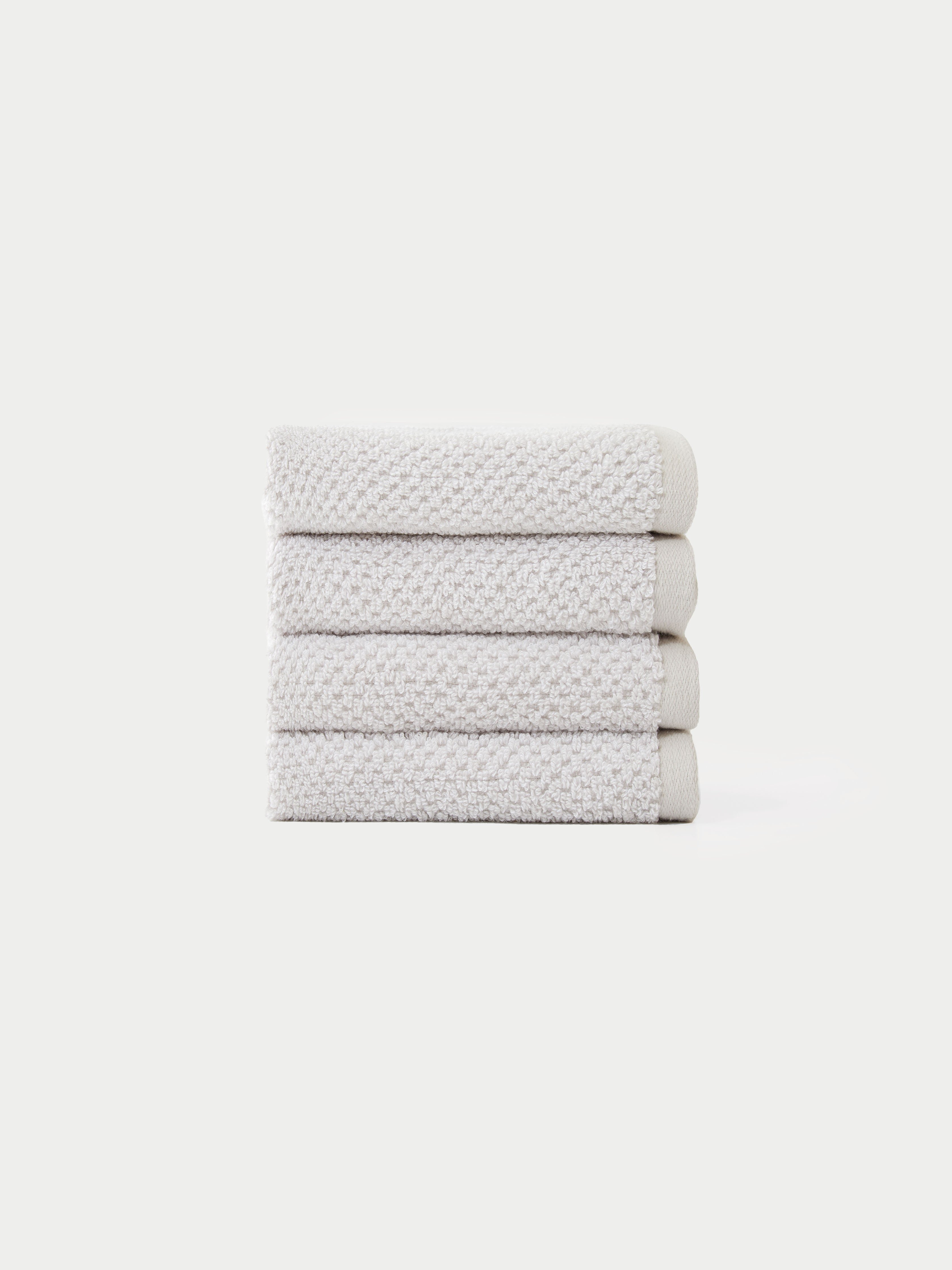 A neatly stacked pile of four folded, light gray textured Nantucket Bath Towels by Cozy Earth is set against a plain white background.