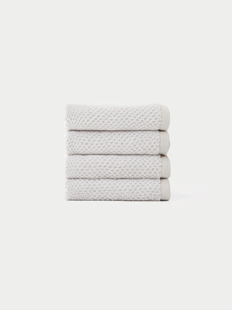 A neatly stacked pile of four folded, light gray textured Nantucket Bath Towels by Cozy Earth is set against a plain white background.