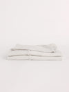 A neatly folded Bamboo Jersey Flat Sheet by Cozy Earth is displayed against a white background. The light gray sheets are tightly stacked, showcasing their smooth texture and clean appearance. |Color:Light Grey