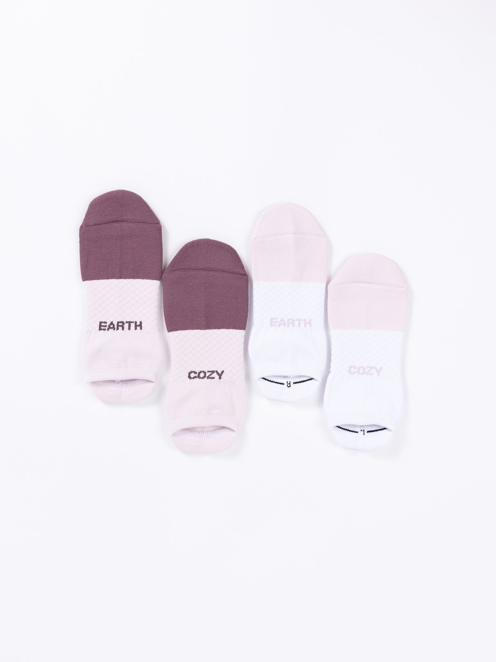 Four pairs of Cozy Earth's Essential Ankle Socks are displayed on a white background. The first pair is dark purple, the second pair is light pink, the third pair is purple with "EARTH" written on the cuff, and the fourth pair is white with "COZY" written on the cuff. 