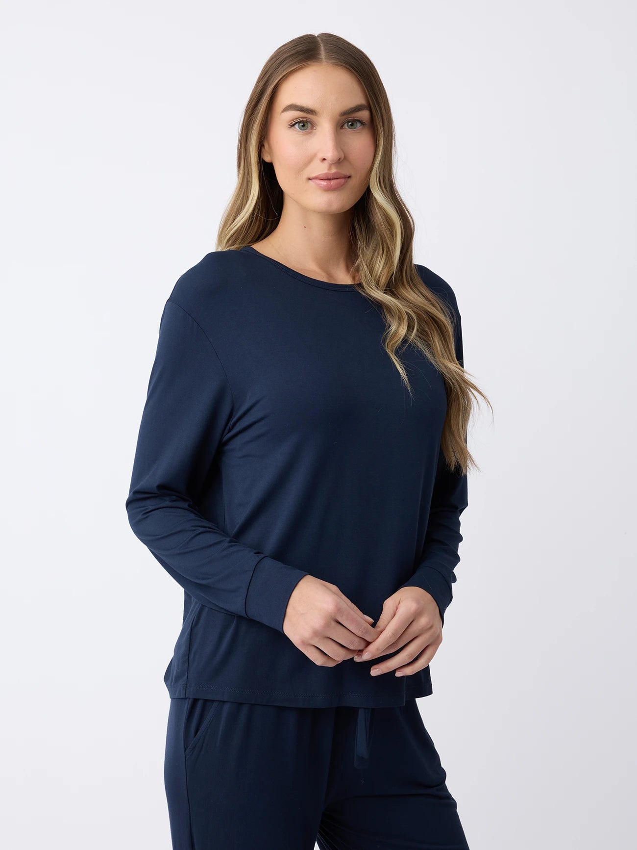 A woman with long hair is wearing a navy blue Women's Stretch Knit Bamboo Long Sleeve Lounge Tee by Cozy Earth, along with matching pants. She stands against a plain white background, looking neutrally at the camera. |Color:Navy