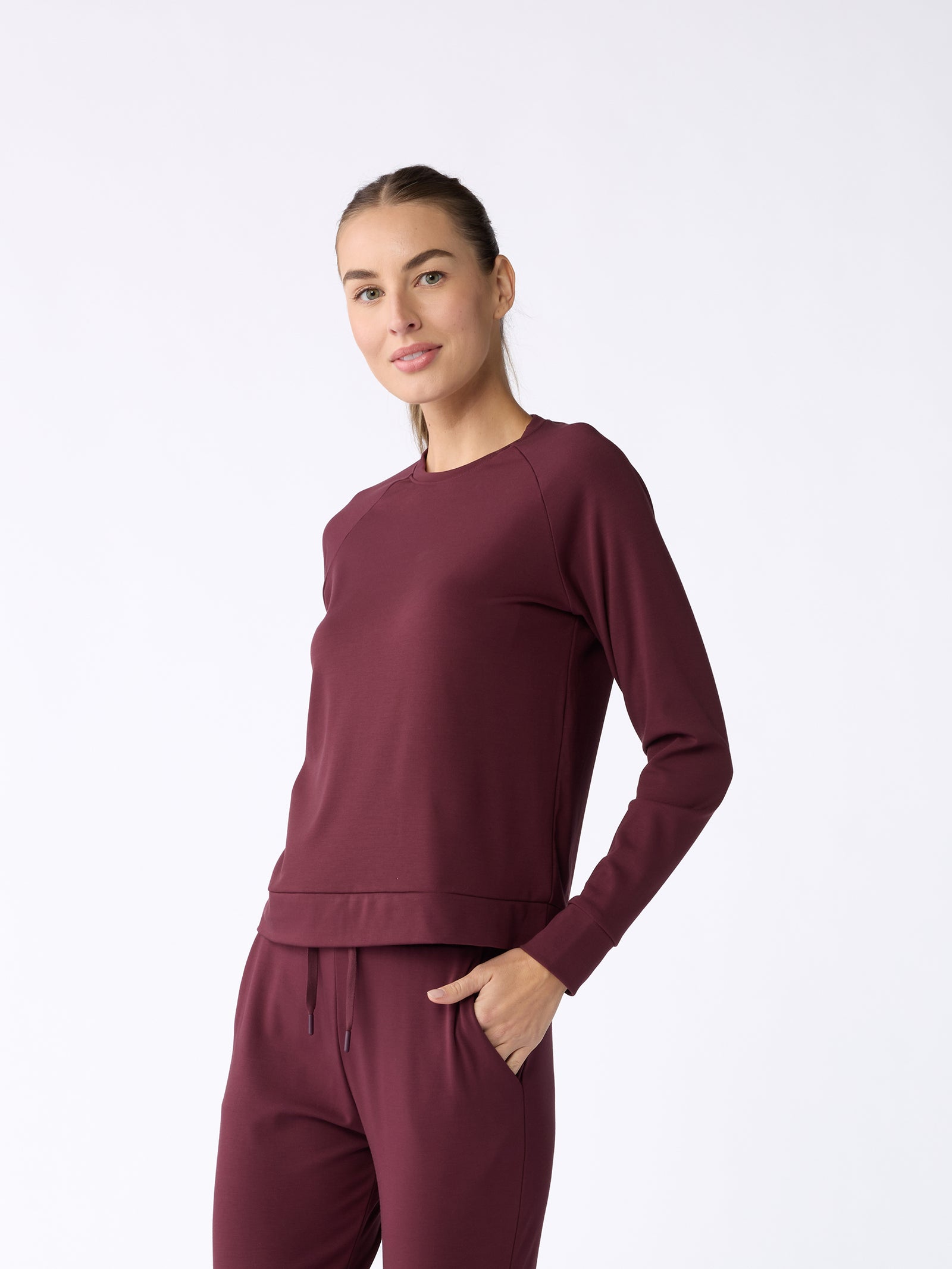 A person wearing the Women's Ultra-Soft Bamboo Pullover Crew by Cozy Earth stands against a plain white background. They have long hair pulled back into a ponytail and are gently smiling at the camera. 