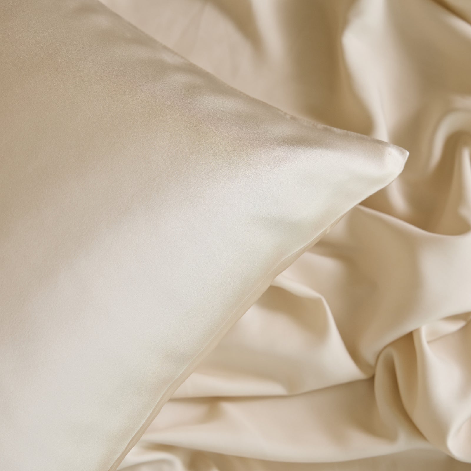 A close-up of Cozy Earth's cream-colored Silk Pillowcase resting on matching silk sheets reveals a smooth and luxurious fabric, with subtle folds creating a soft texture. 