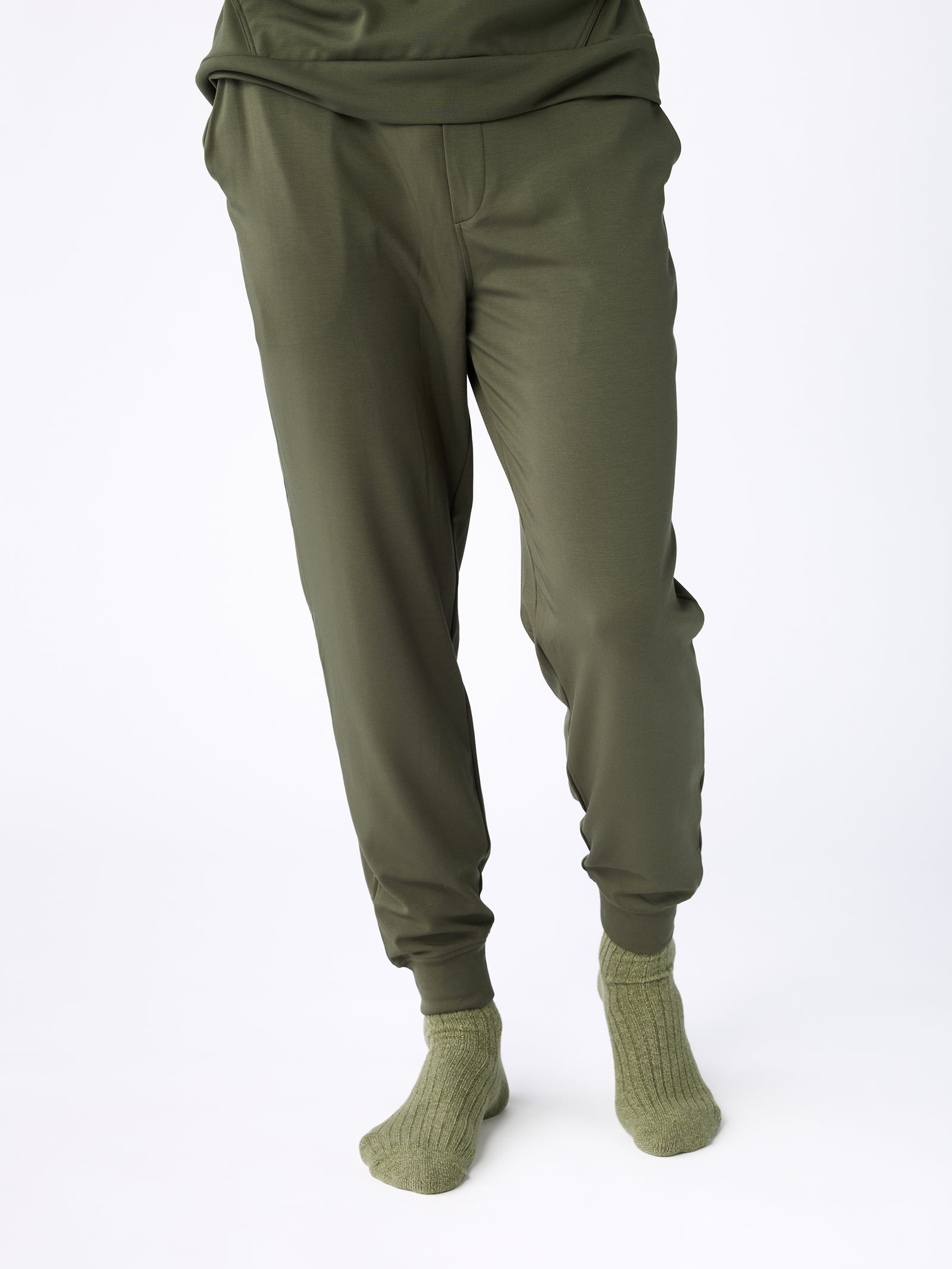 A person wearing jogger pants in olive green, paired with matching socks, stands against a plain white background. The pants have a relaxed fit and feature a drawstring. However, the Men's Ultra-Soft Bamboo Pullover Crew from Cozy Earth is not visible as the upper body and face are not shown. 