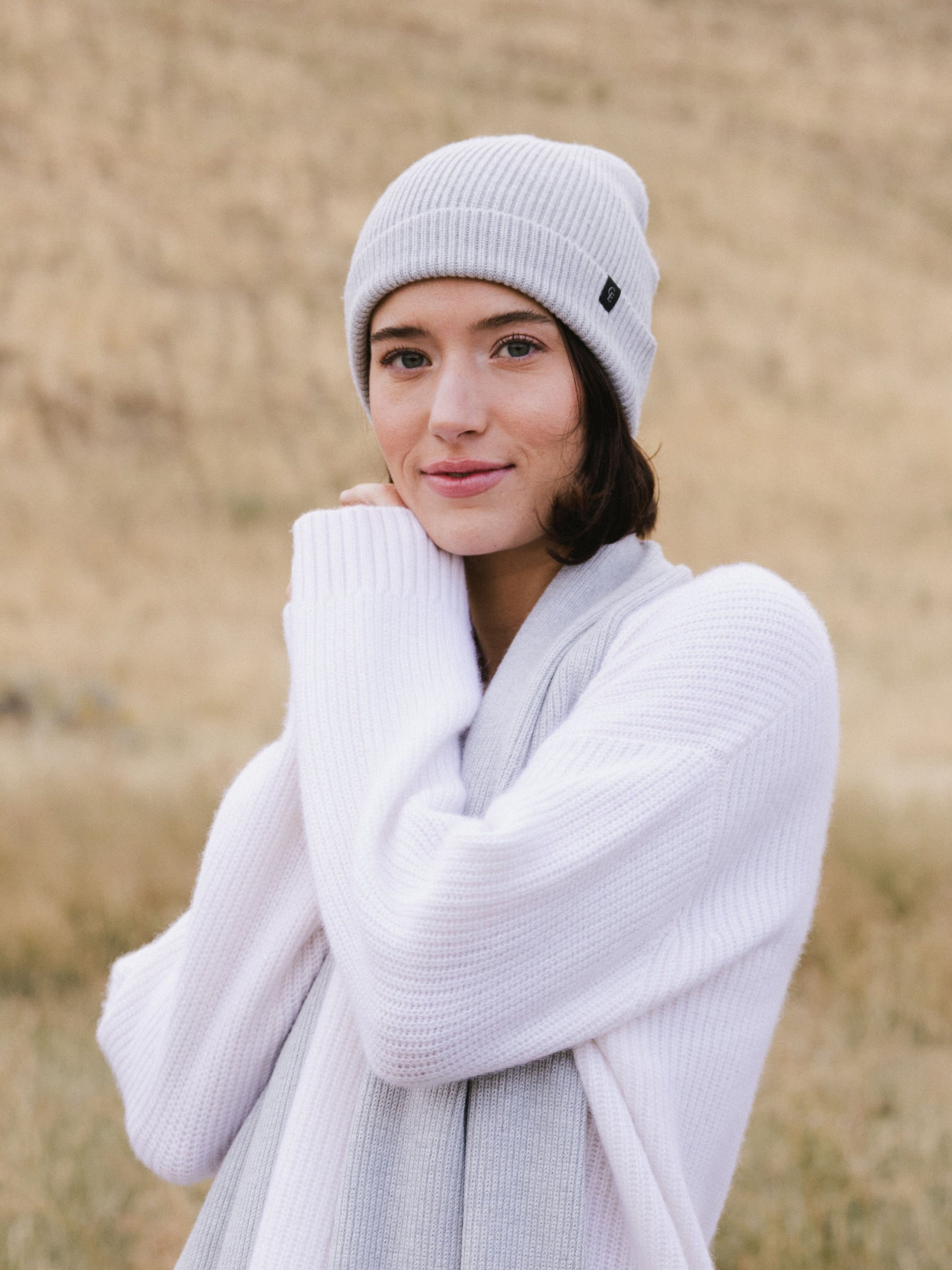 Woman wearing a light gray knit beanie and scarf in a field 
