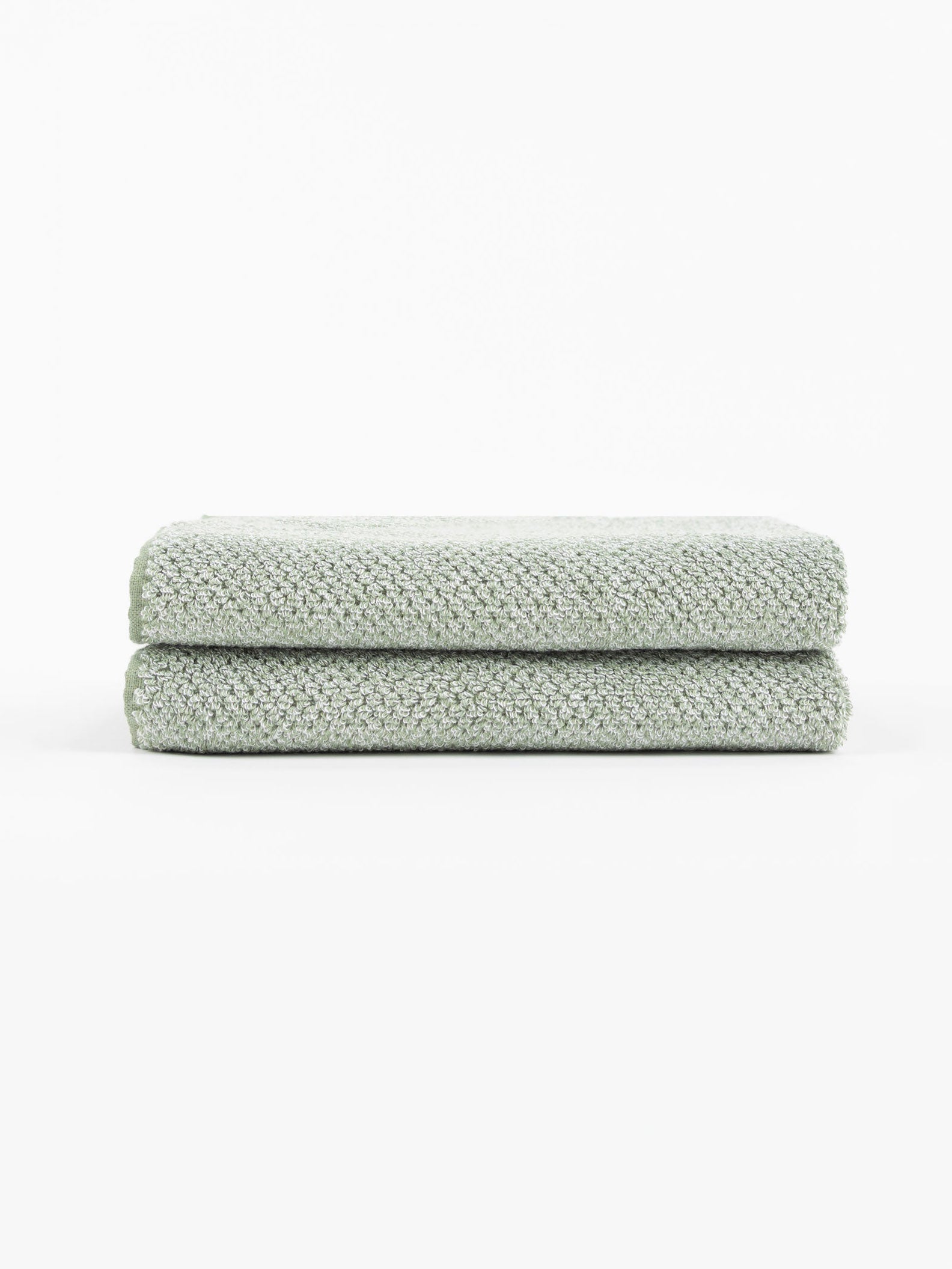 Two Nantucket Bath Towels by Cozy Earth, in a light green textured finish, are neatly folded and stacked on a white surface with a plain white background.