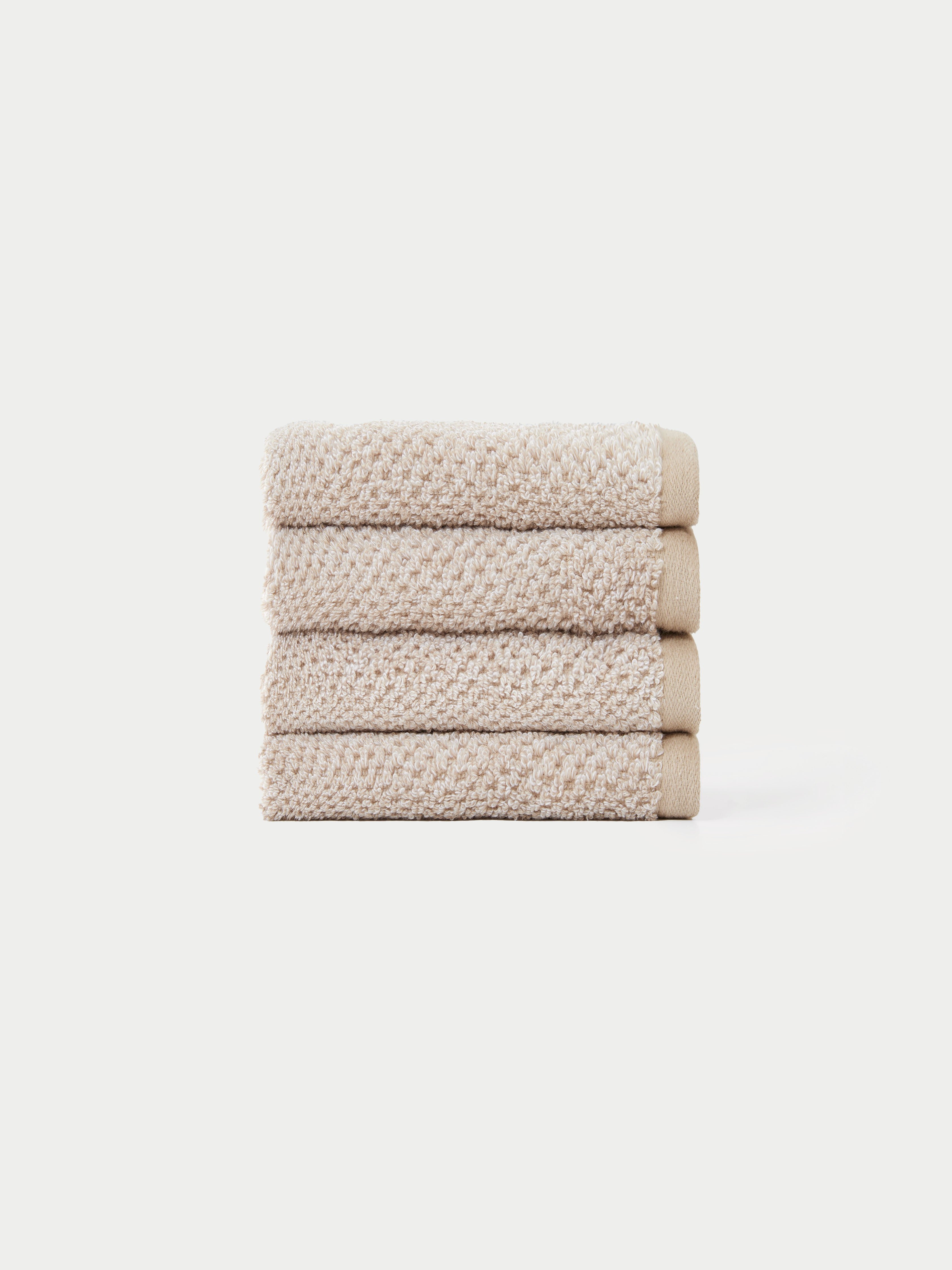A neatly stacked pile of four beige, textured hand towels from the Cozy Earth Nantucket Bath Towel Set is displayed against a plain white background.