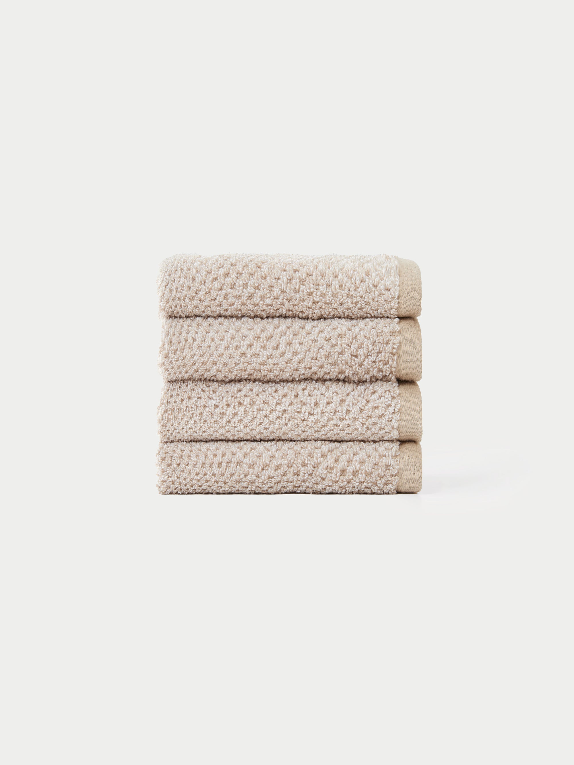 A neatly stacked pile of four beige, textured hand towels from the Cozy Earth Nantucket Bath Towel Set is displayed against a plain white background.