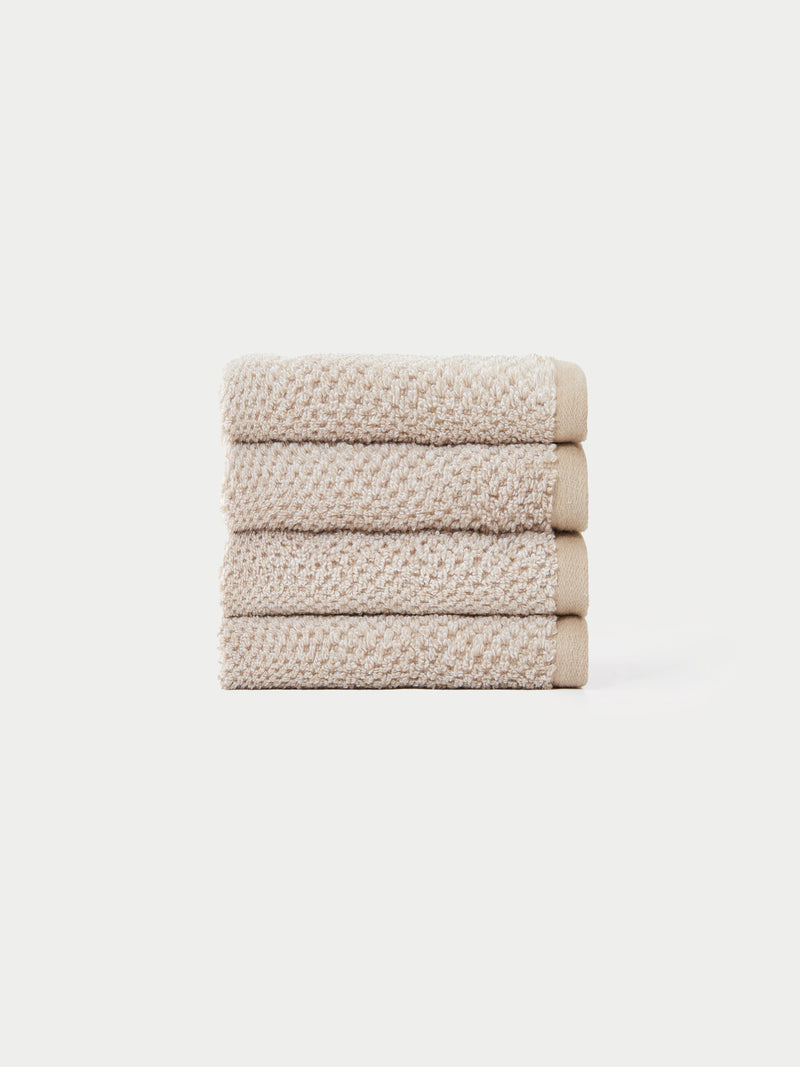 A neatly stacked pile of four beige, textured hand towels from the Cozy Earth Nantucket Bath Towel Set is displayed against a plain white background.