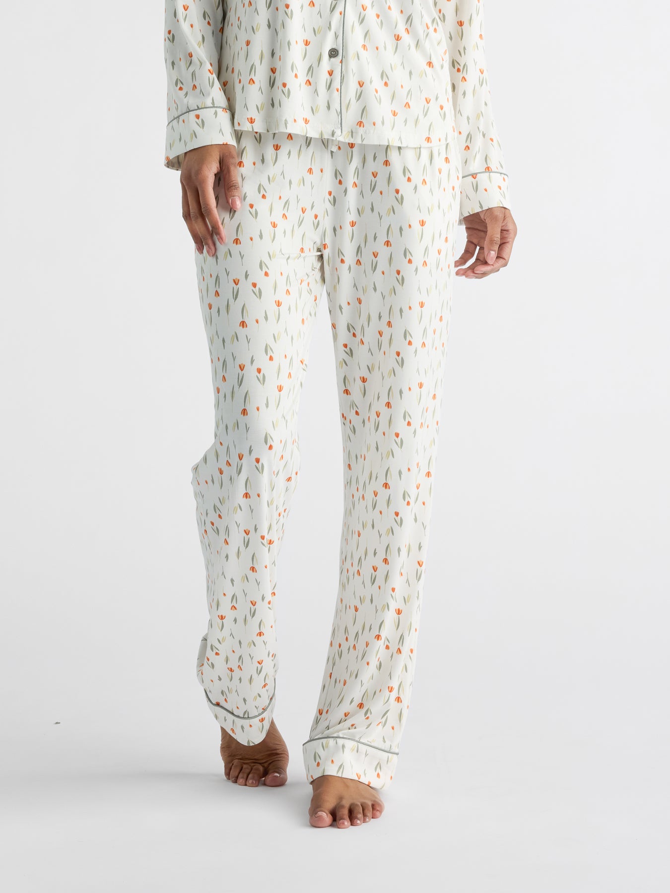 A person models HIDE's Women's Bamboo Stretch-Knit Pajama Pant, featuring light-colored fabric with a small, colorful pattern. The outfit includes long sleeves and pants, shown from shoulders to feet against a plain white background. 