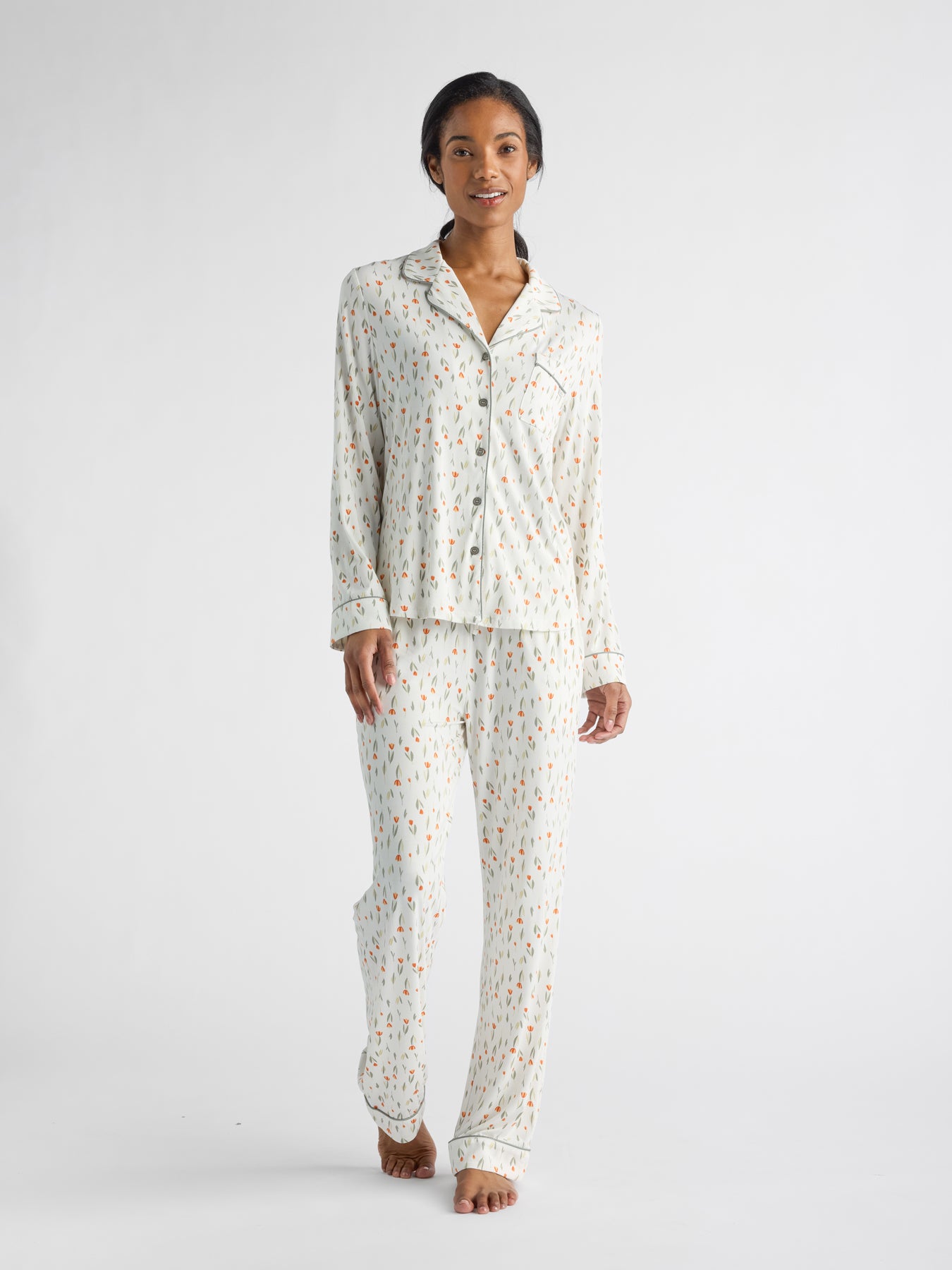 A person stands barefoot on a white background, smiling and relaxed, wearing Cozy Earth's Women's Bamboo Stretch-Knit Long Sleeve Pajama Set featuring a scattered print pattern. |Color:Sienna Tulips