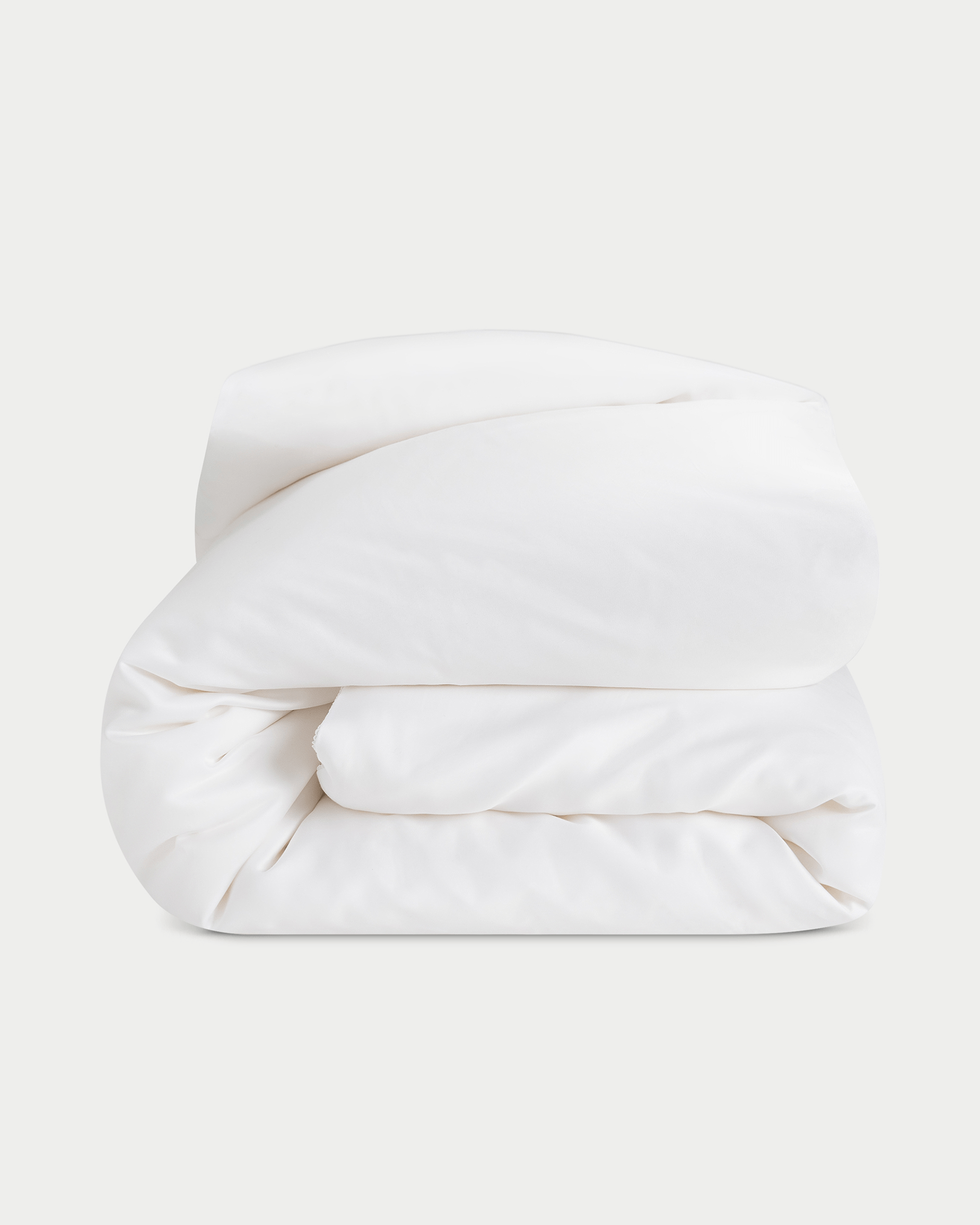 A neatly folded, fluffy Silk Comforter by Cozy Earth is placed against a plain light background. The fabric appears smooth and soft, highlighting its plush and inviting texture.