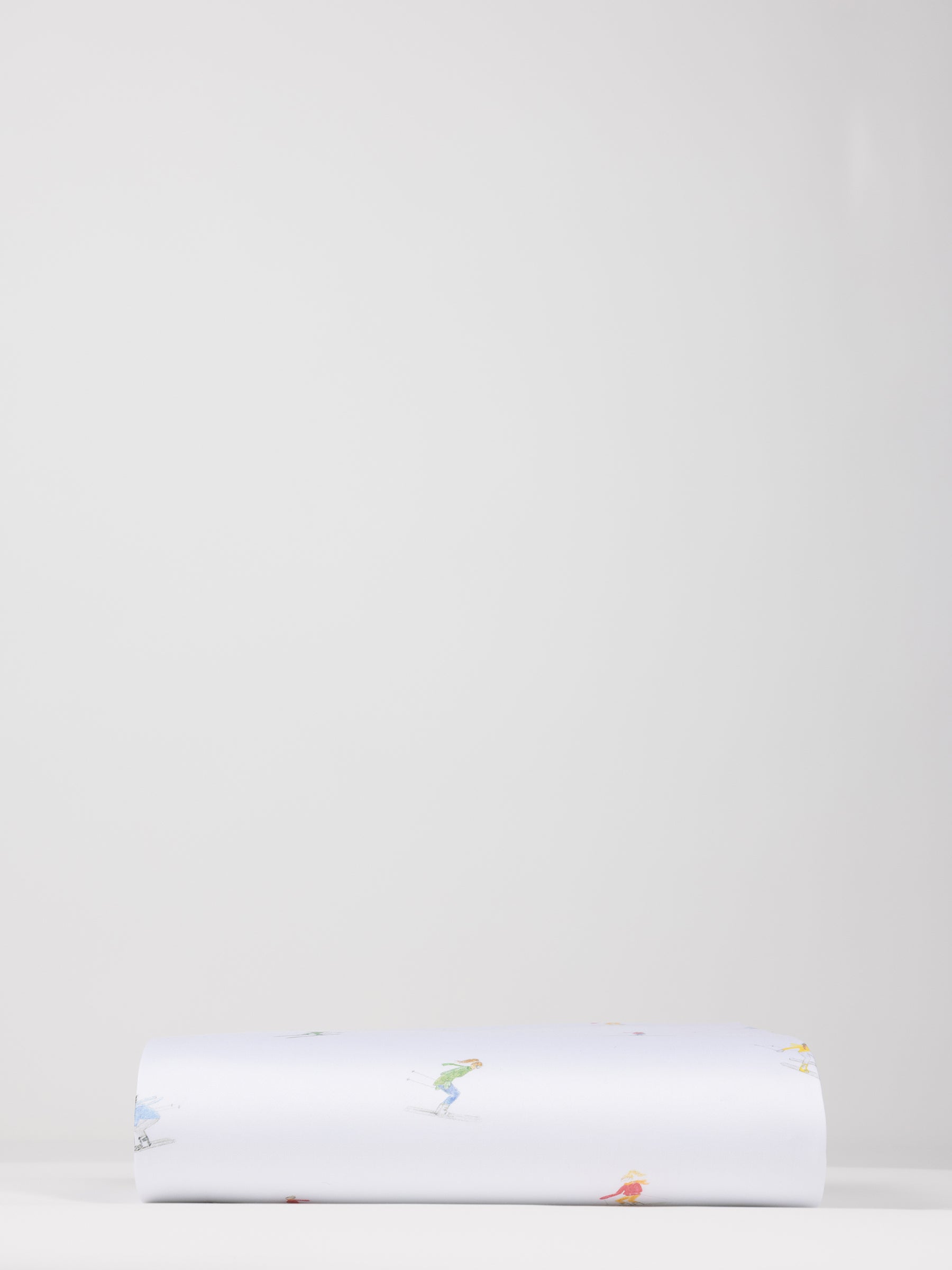 A neatly folded Bamboo Duvet Cover from Cozy Earth is laid flat against a plain, light gray background. The cover is predominantly white with small, colorful illustrations or designs scattered across its surface. |Color:Skiers