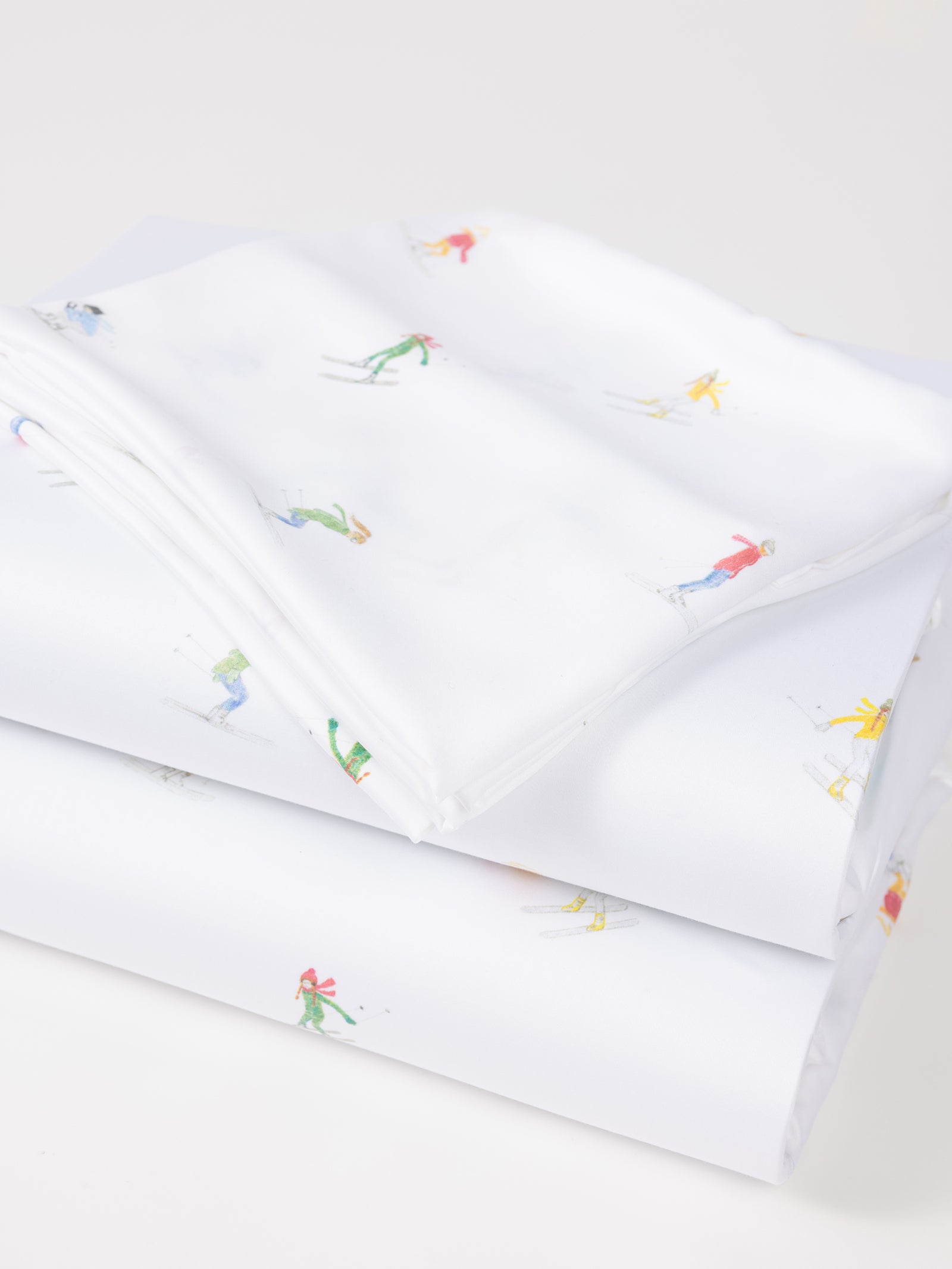 A neatly folded Bamboo Sheet Set by Cozy Earth, featuring colorful skier illustrations against a plain white background. The skiers are showcased in various poses and vibrant outfits. 