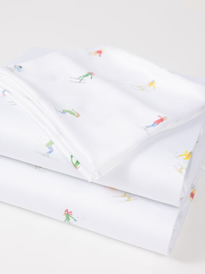 A neatly folded Bamboo Sheet Set by Cozy Earth, featuring colorful skier illustrations against a plain white background. The skiers are showcased in various poses and vibrant outfits. |Color:Skiers